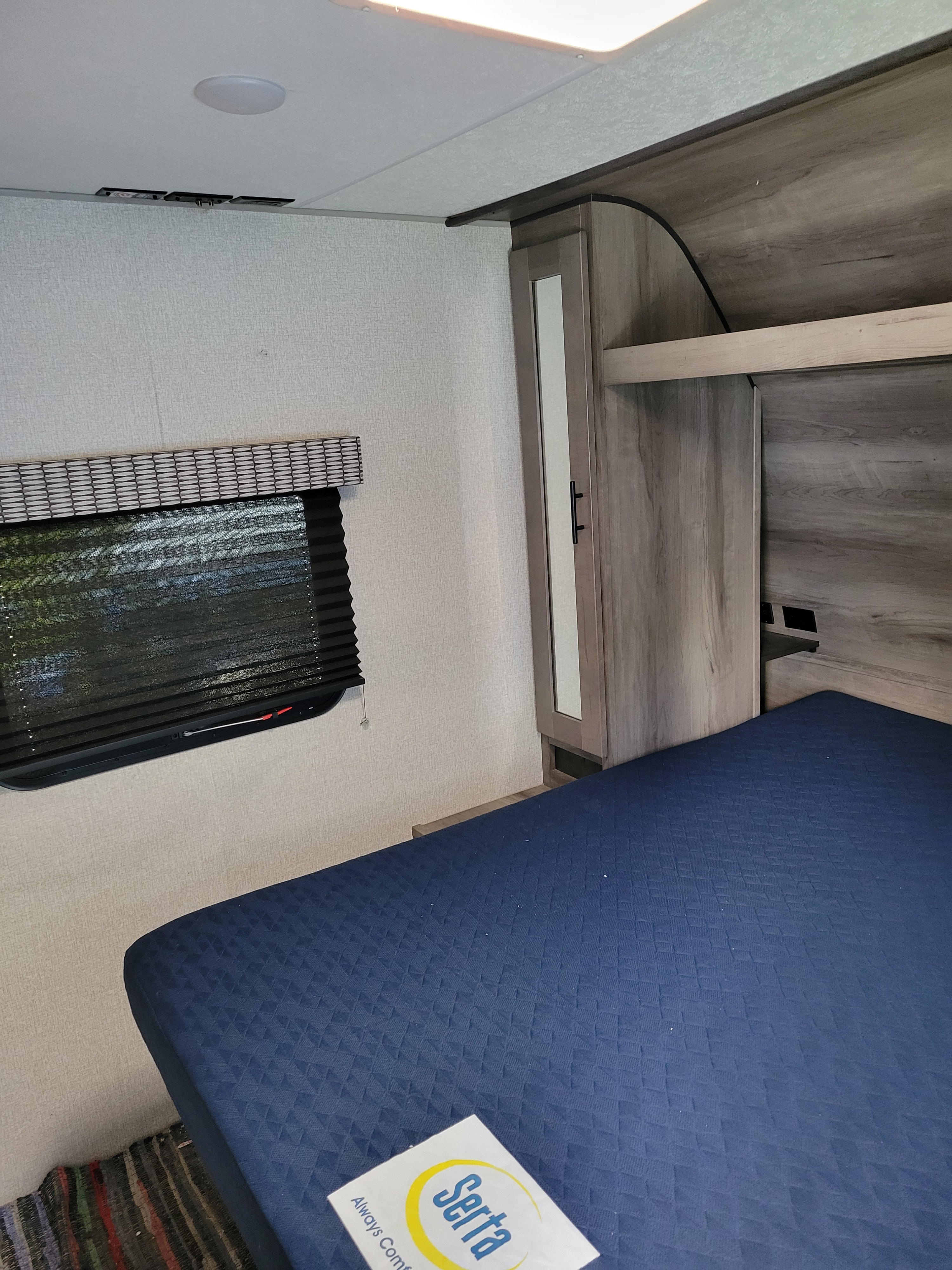 Cozy RV rental bedroom featuring a blue Serta mattress, mirrored wardrobe, and pleated window blind.. KZ Confluence 2022