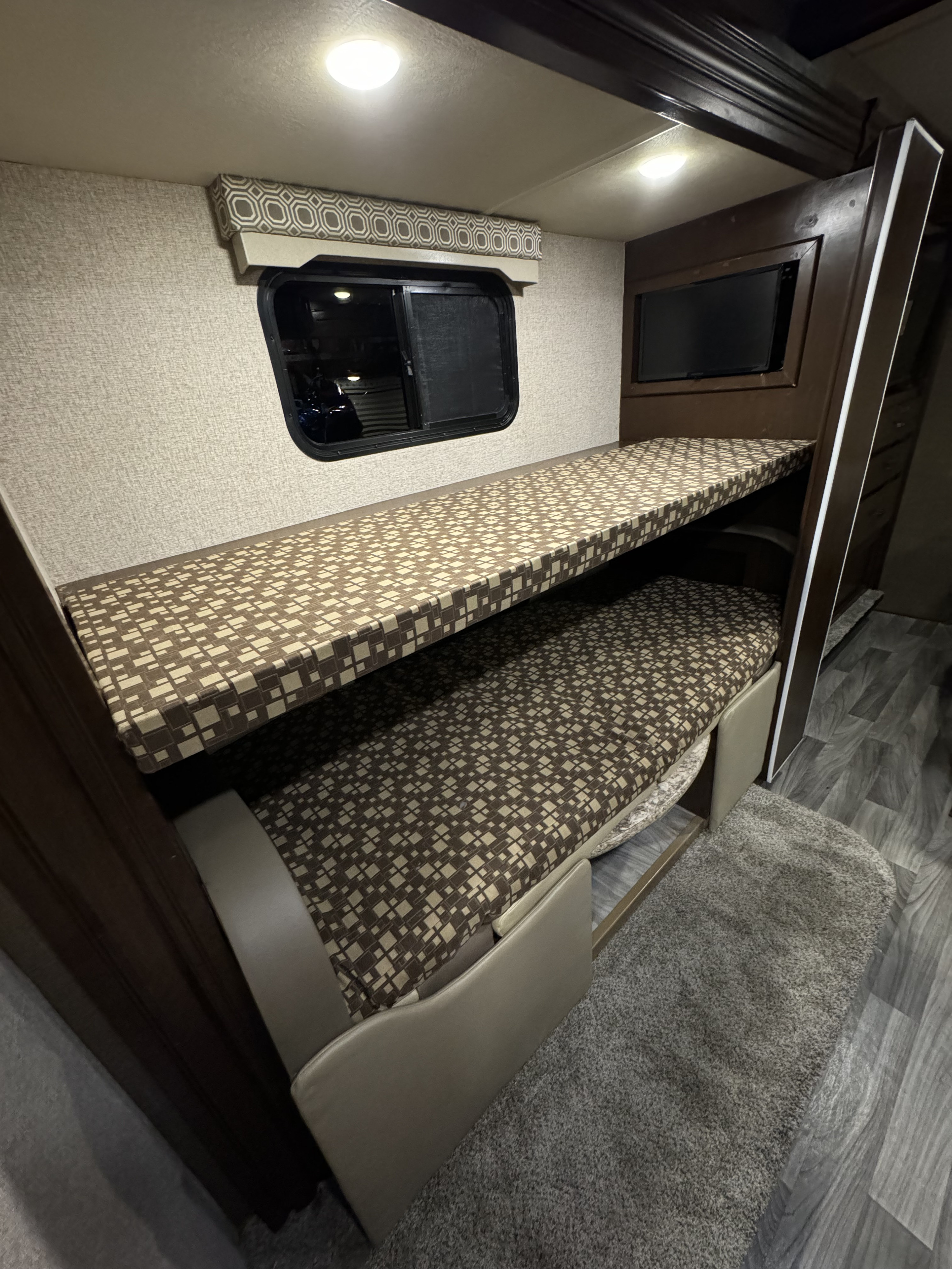 RV rental interior featuring comfortable bunk beds with patterned cushions, window, & TV for a cozy travel experience.. Thor Four Winds 2019