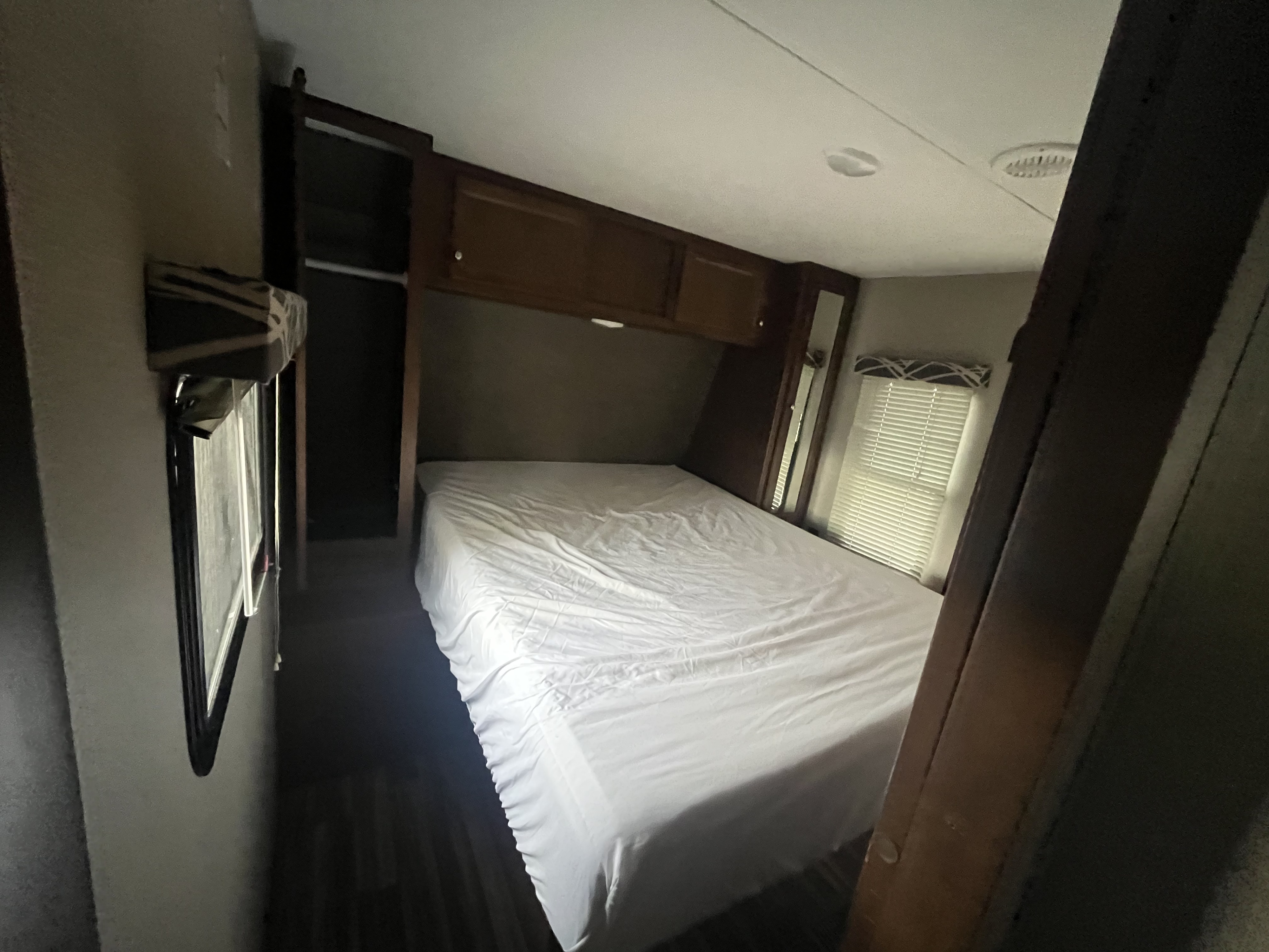 RV rental bedroom featuring a large white bed, overhead cabinets, and a window, ideal for comfortable travel.. Keystone RV Hideout Luxury 2017