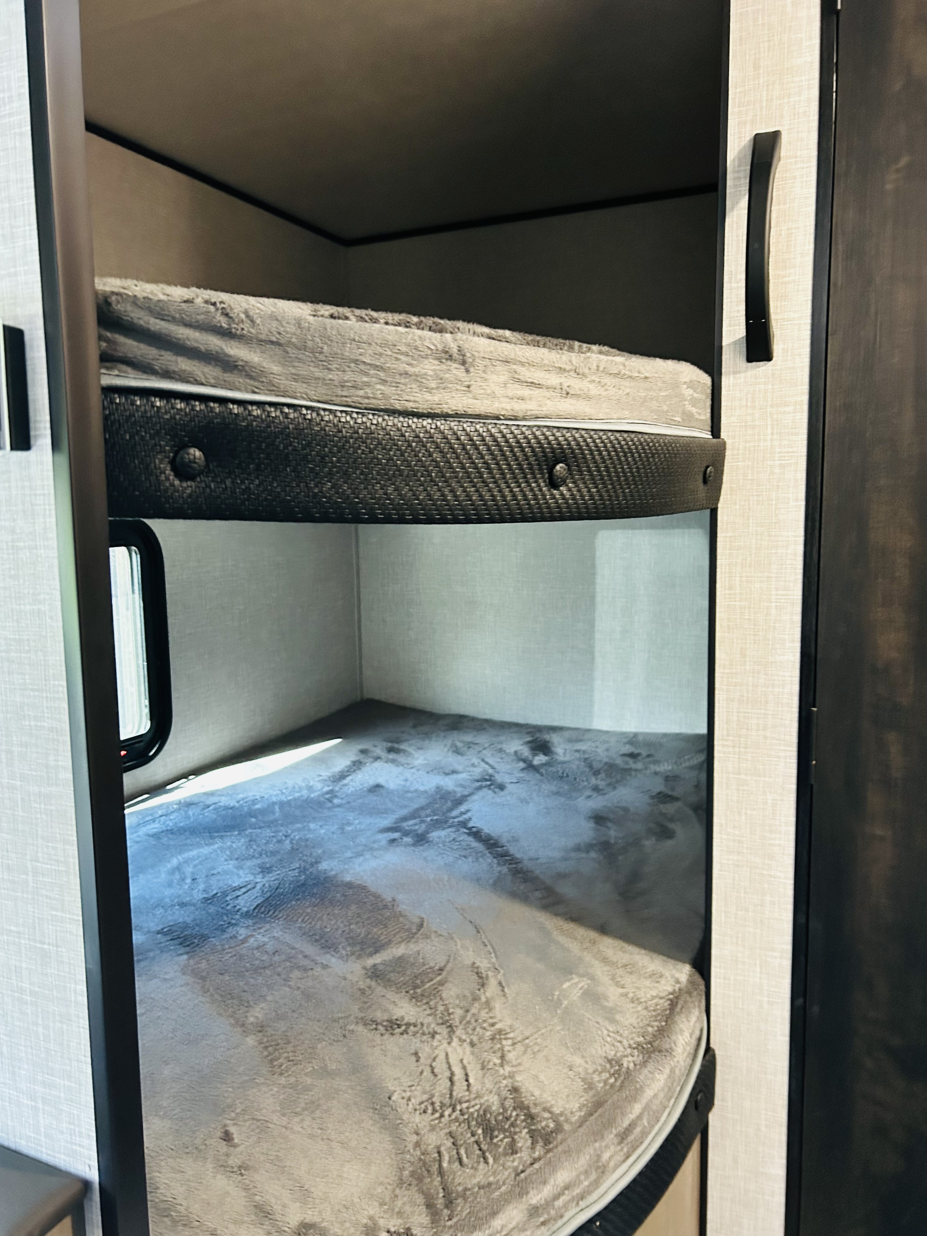 Cozy bunk beds in an RV rental, featuring soft grey blankets and a window. An ideal compact sleeping area for travelers.. Jayco Jay flight Slx 2024