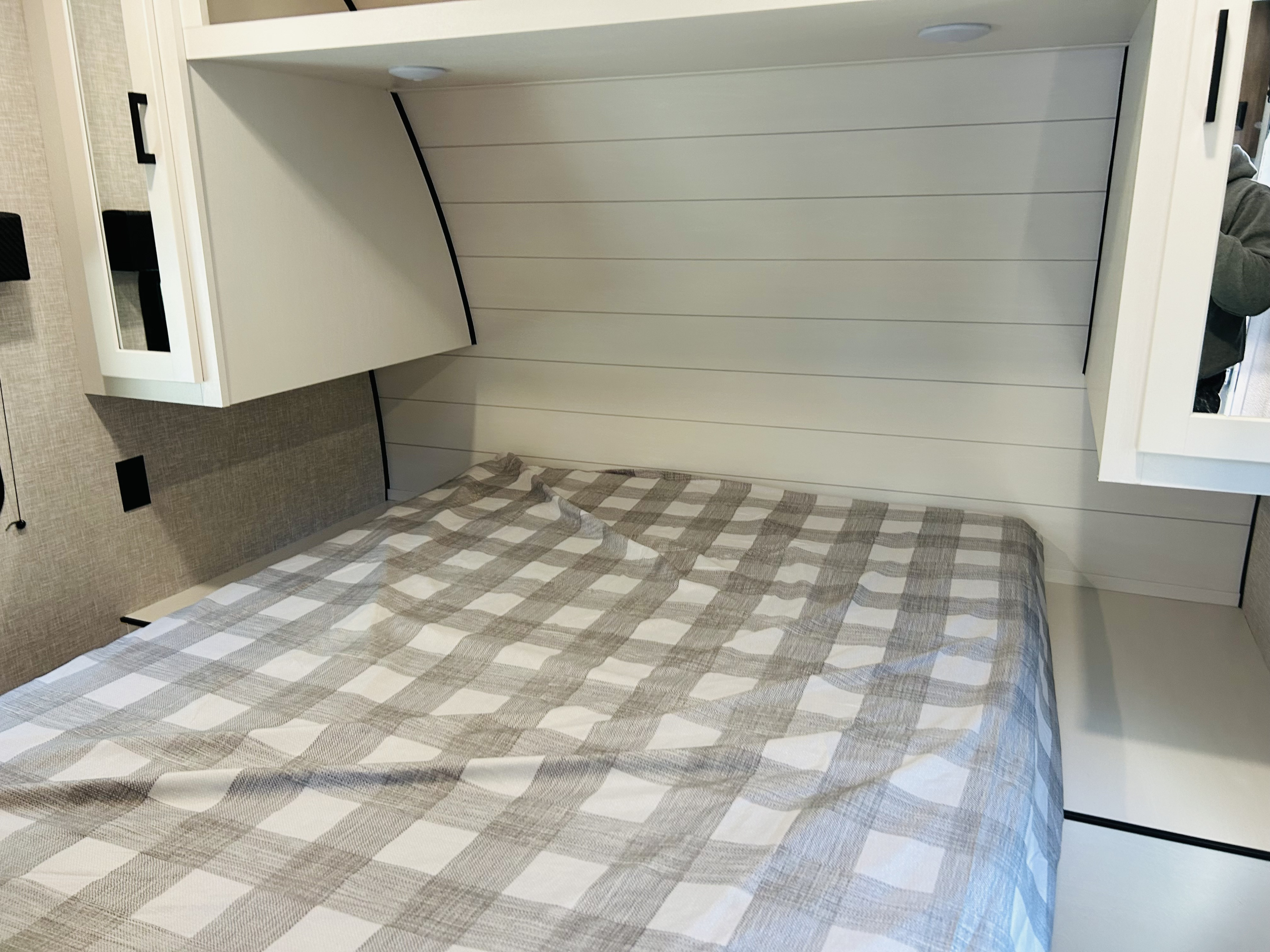 Inside an RV rental: a compact bedroom with a comfy bed, plaid bedding, shiplap wall, and storage cabinets.. Jayco Jay flight Slx 2024
