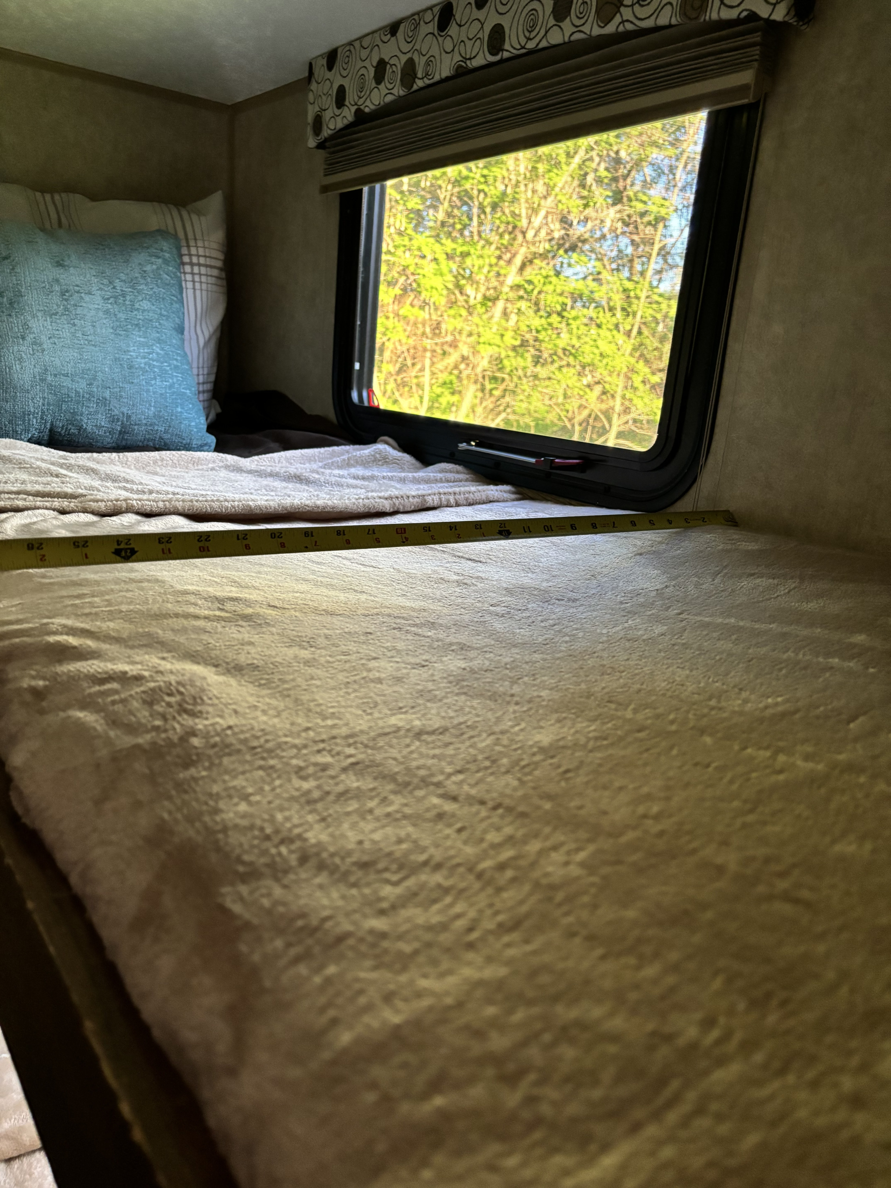 Measuring the width of a bunk bed inside an RV rental. A tape measure lies across the cozy blanket and pillow, with a window view.. Coachmen Clipper 2017