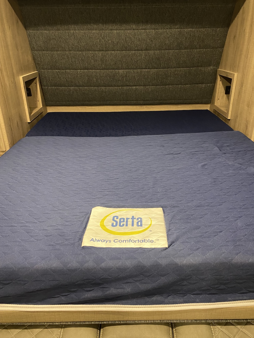 Cozy sleeping area in an RV rental featuring a dark blue Serta mattress & wood-toned built-in storage. Ready for comfortable travel.. Grand Design Imagine XLS 2022