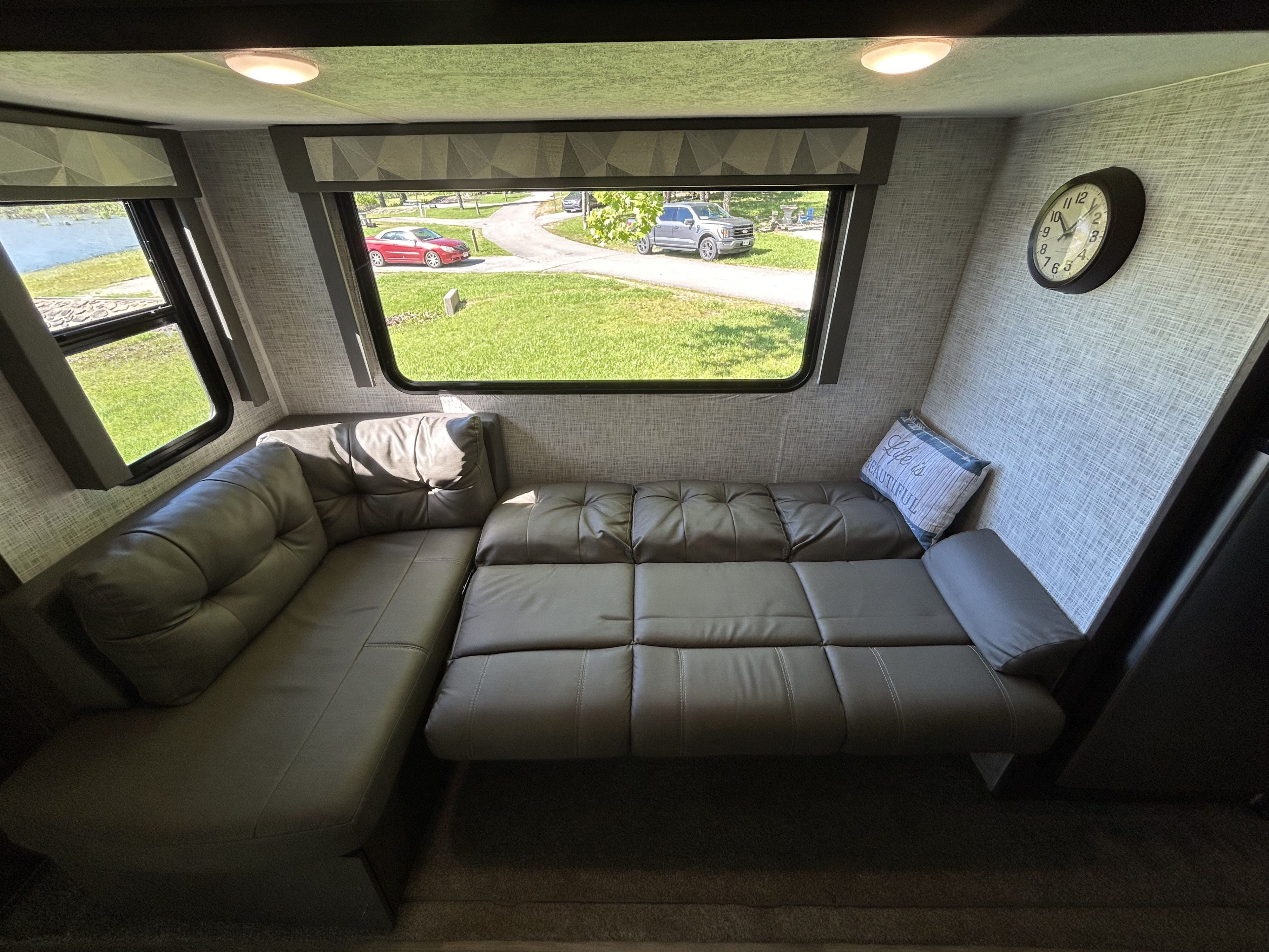 Spacious RV rental interior featuring an L-shaped sofa, large windows with outdoor views of nature, and a tranquil lake.. Forest River Salem 2020