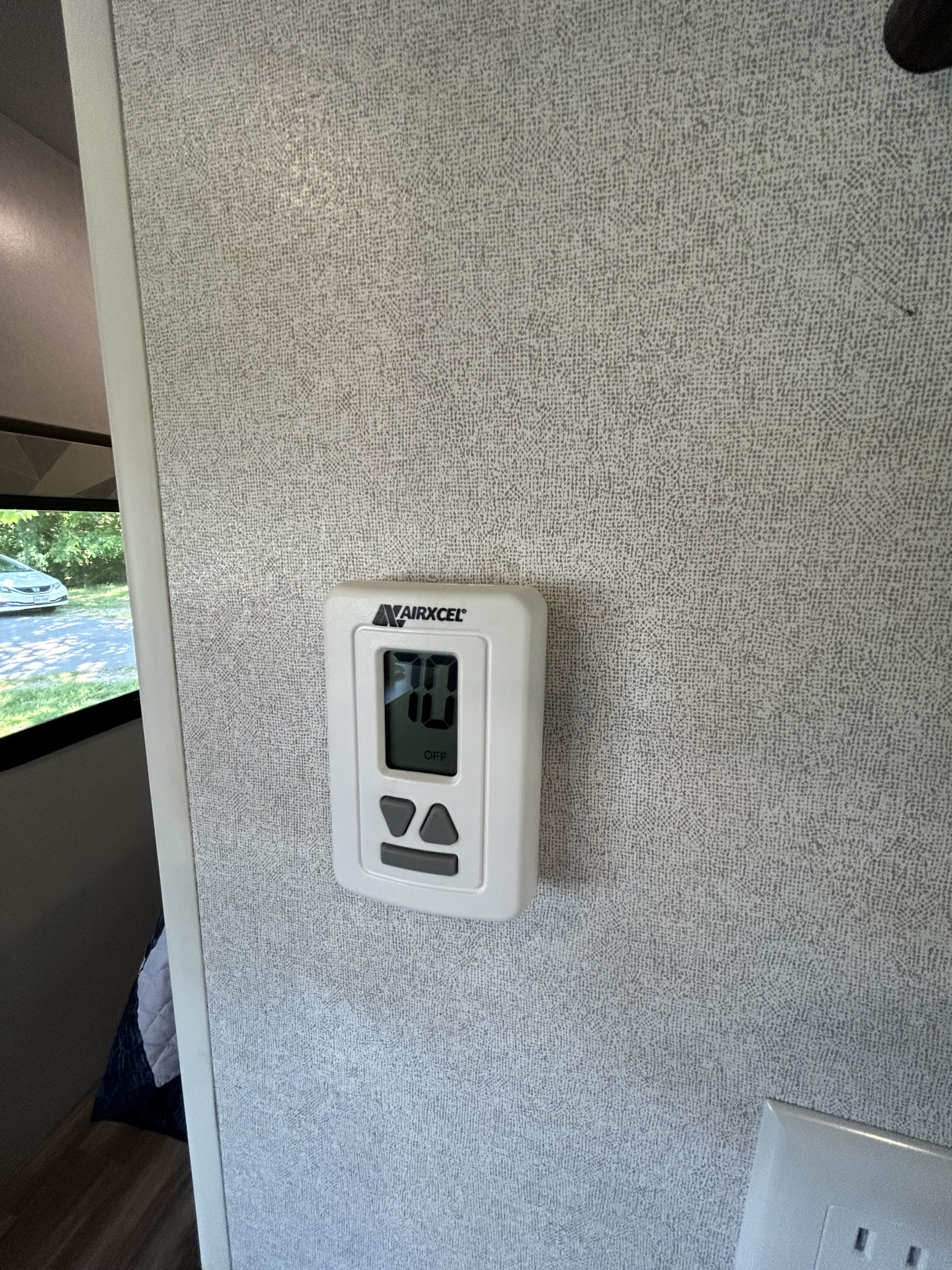 This RV rental's Airxcel thermostat displays 70 degrees and is currently OFF, mounted on a textured interior wall, with a car visible outside.. Forest River Salem 2020
