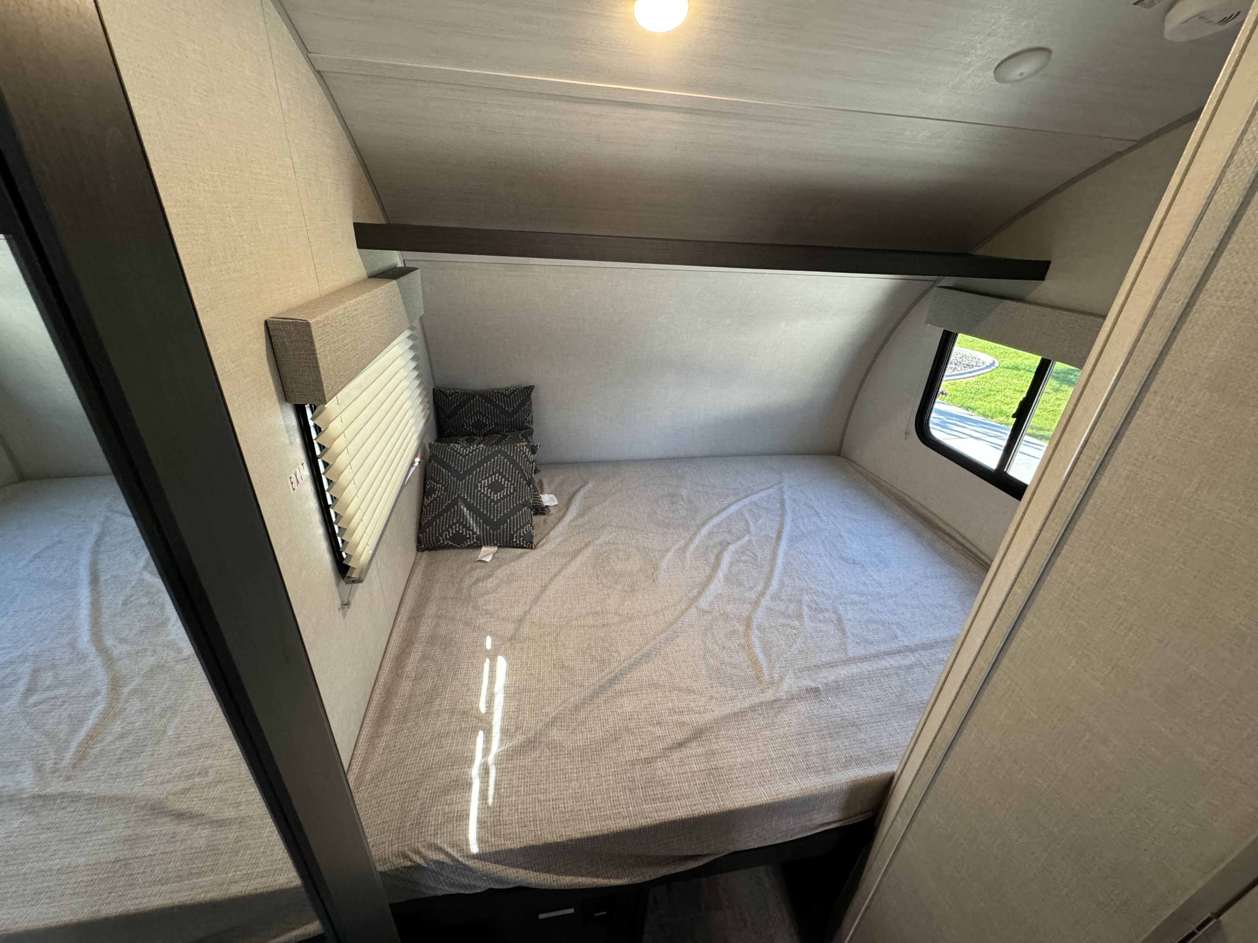 This inviting RV rental bedroom features a cozy bed with neutral linens, patterned pillows, a window, and overhead beam storage.. R-Pod R-Pod Trailer 2024