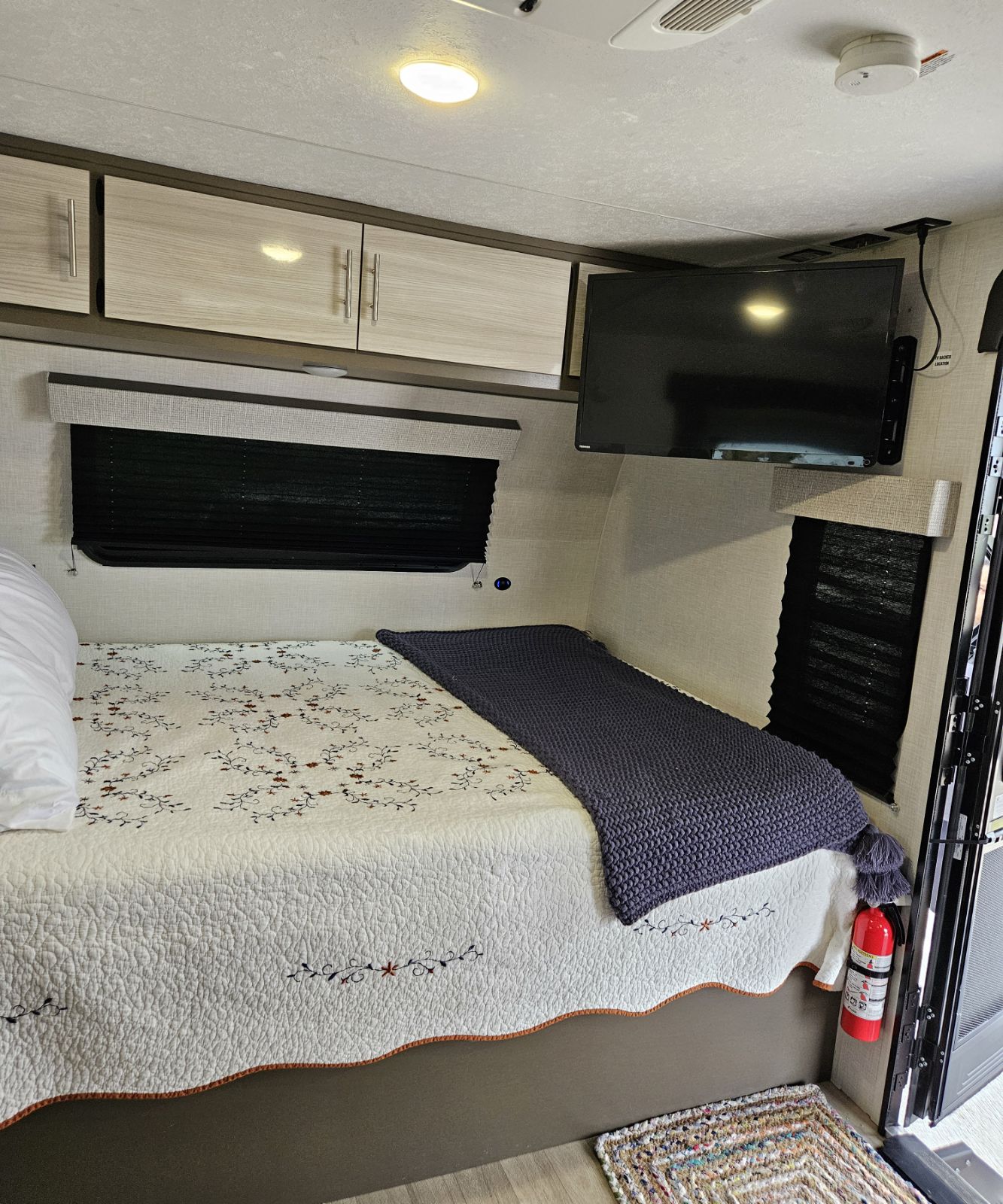 Safety-equipped RV rental interior: cozy bed, TV, storage cabinets, window blinds, and a fire extinguisher for peace of mind.. KZ Escape 2023