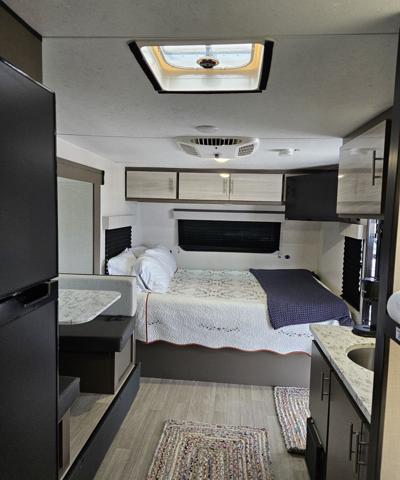 Inside an RV rental: a bright, compact interior with a bed, kitchen area, dinette, and ceiling vent, showing functional living.. KZ Escape 2023