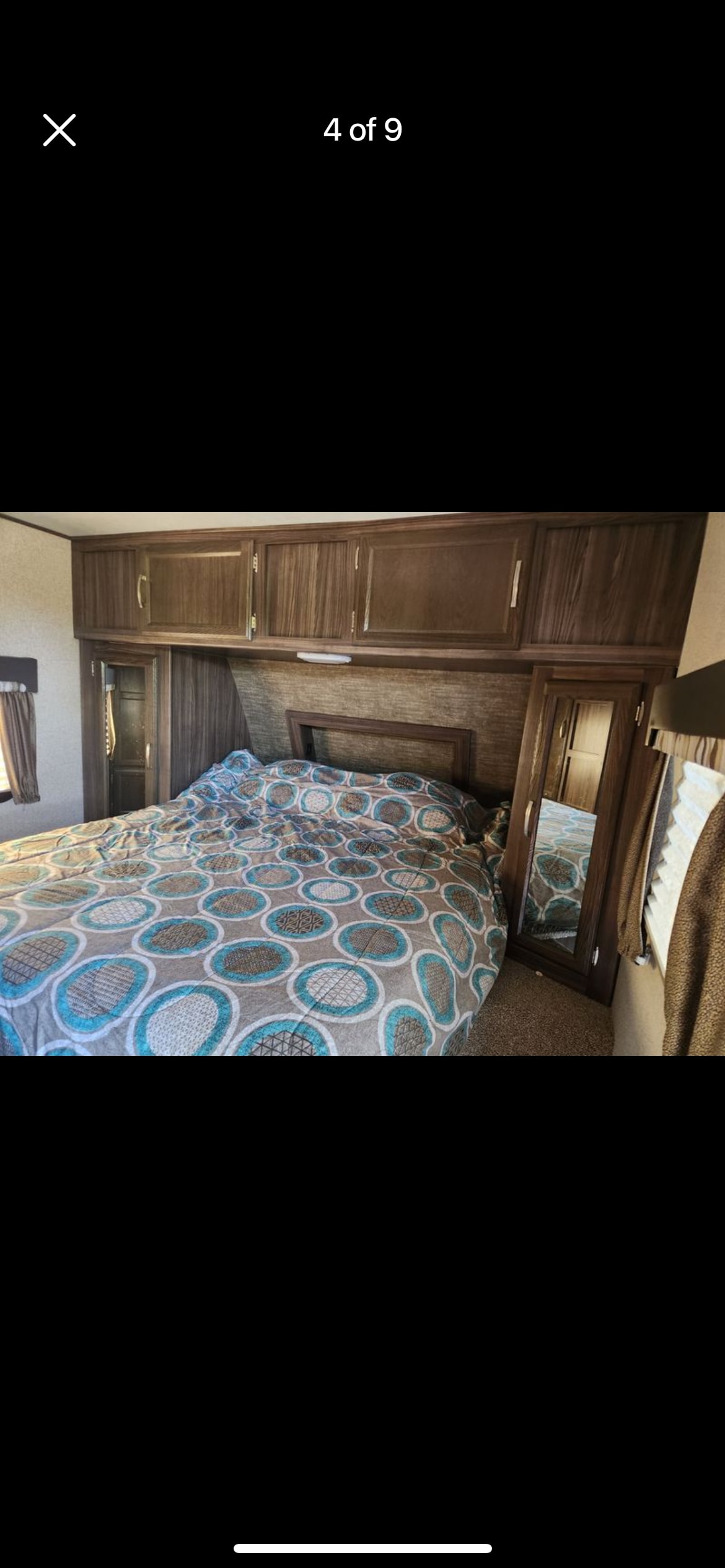 RV bedroom showing a bed with a teal and brown patterned comforter, wood overhead cabinets, and mirrored wardrobes for your rv rental.. Coachmen Apex 2019