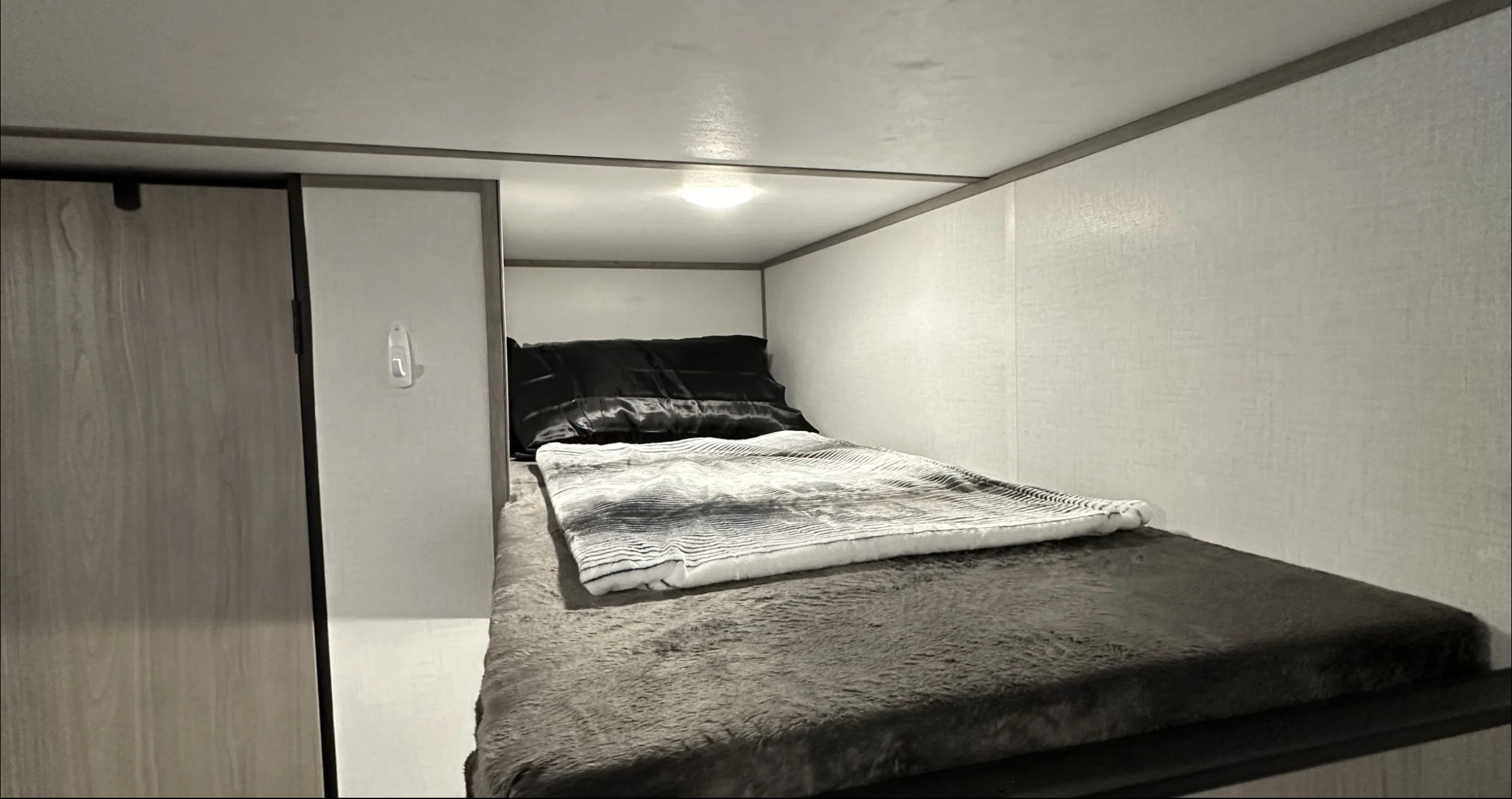 Compact RV rental bunk bed featuring a cozy, dark furry mattress, black pillow, and striped blanket. Small ceiling light above.. Dutchmen Coleman Lantern LT 2023