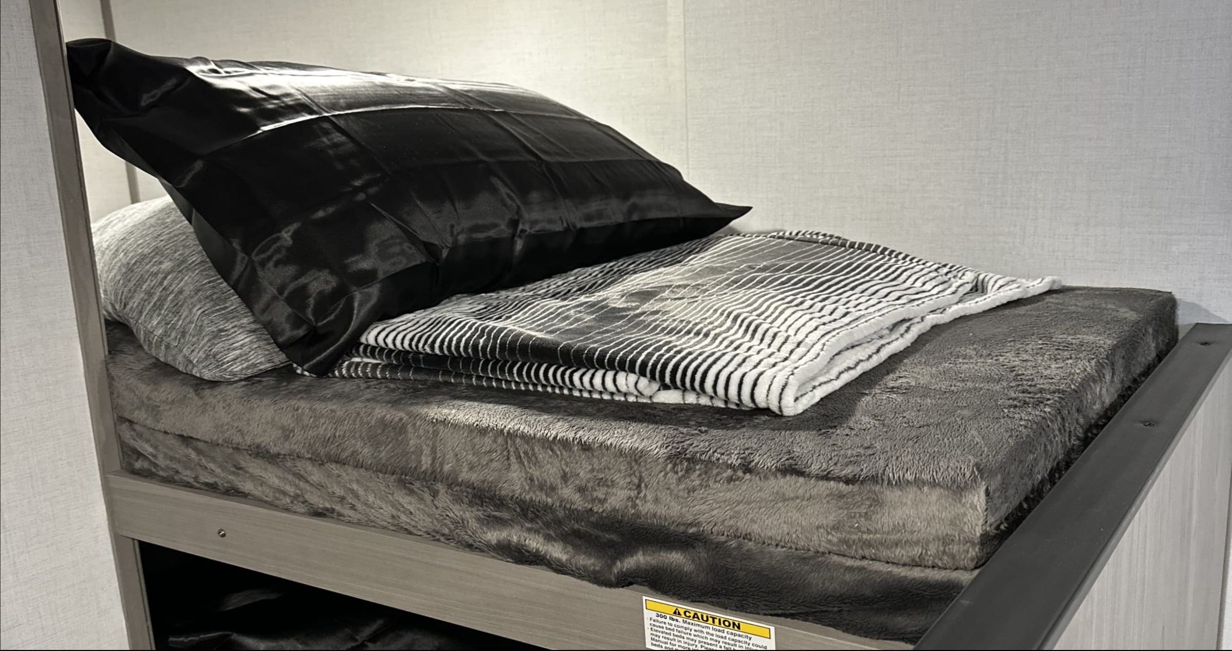 An RV rental bunk bed with a cozy grey mattress, pillows, and striped blanket, ready for comfortable sleeping.. Dutchmen Coleman Lantern LT 2023