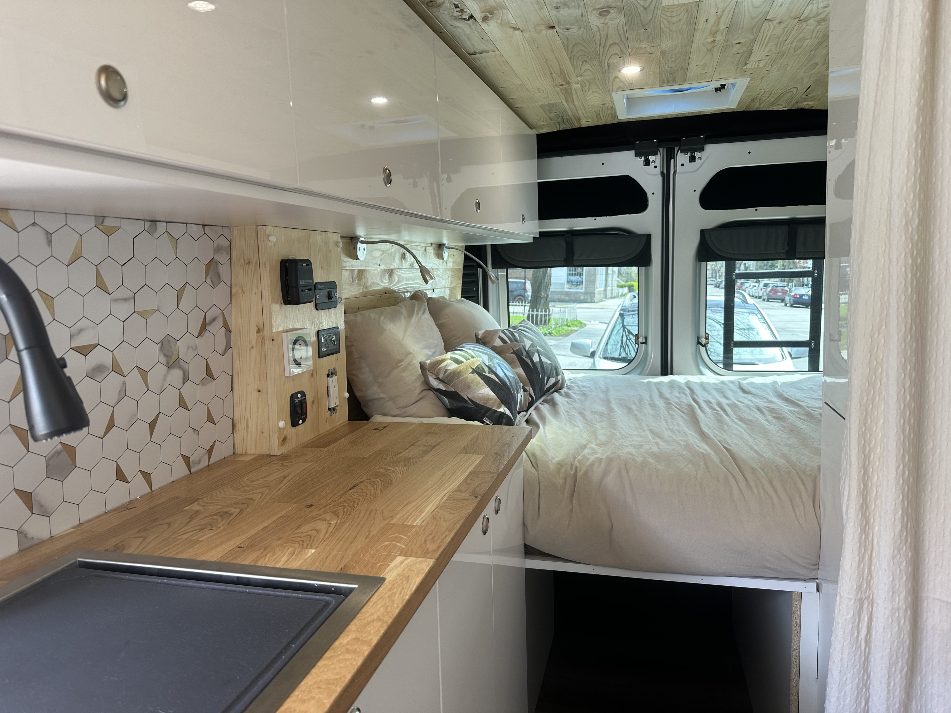 View of a well-designed rv rental interior, showing kitchen with wood counters, bed, and rear windows.. Dodge Promaster 2023
