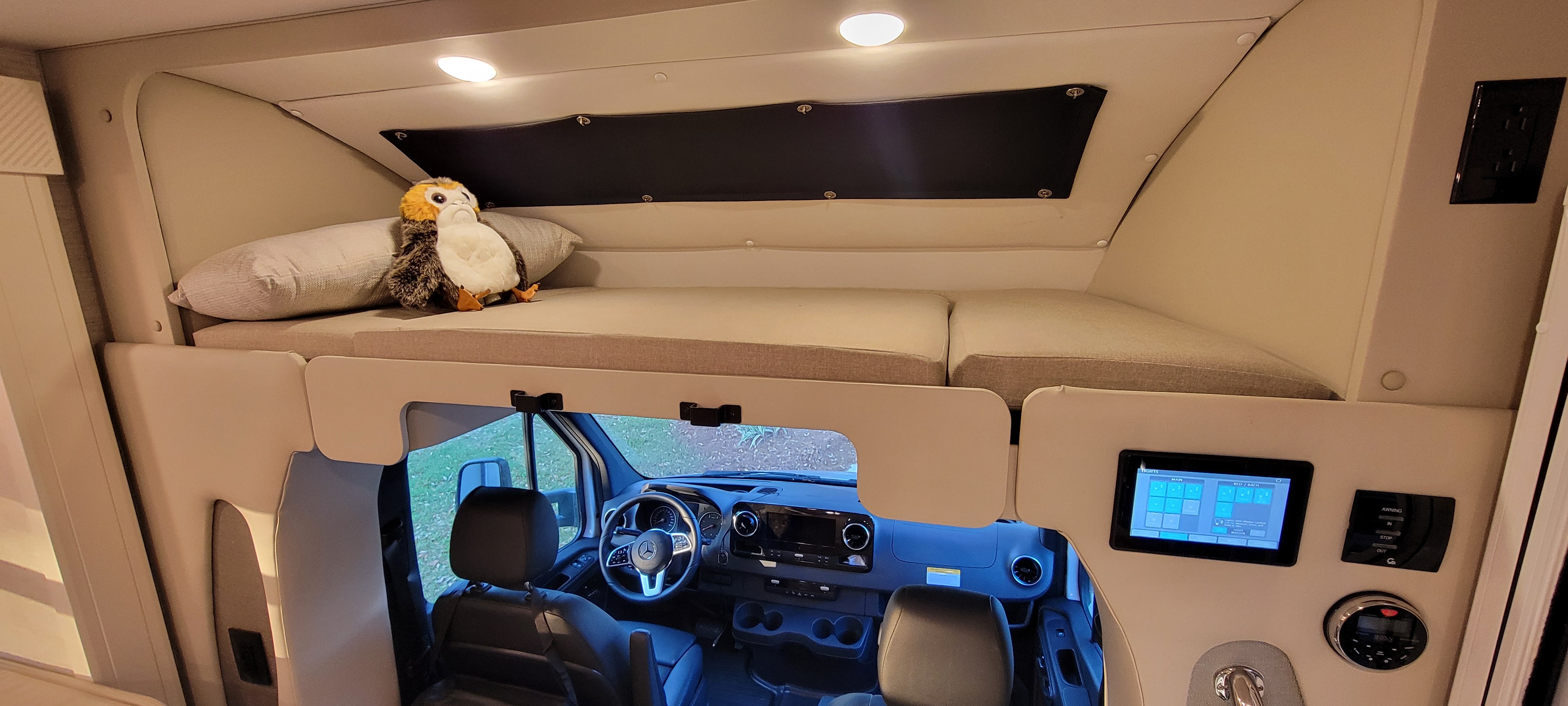 Inside an RV rental: a cozy cab-over bunk bed with a Porg toy, overlooking the Mercedes-Benz driver's cockpit and controls.. Wayfarer Wayfarer Motorhome 2024