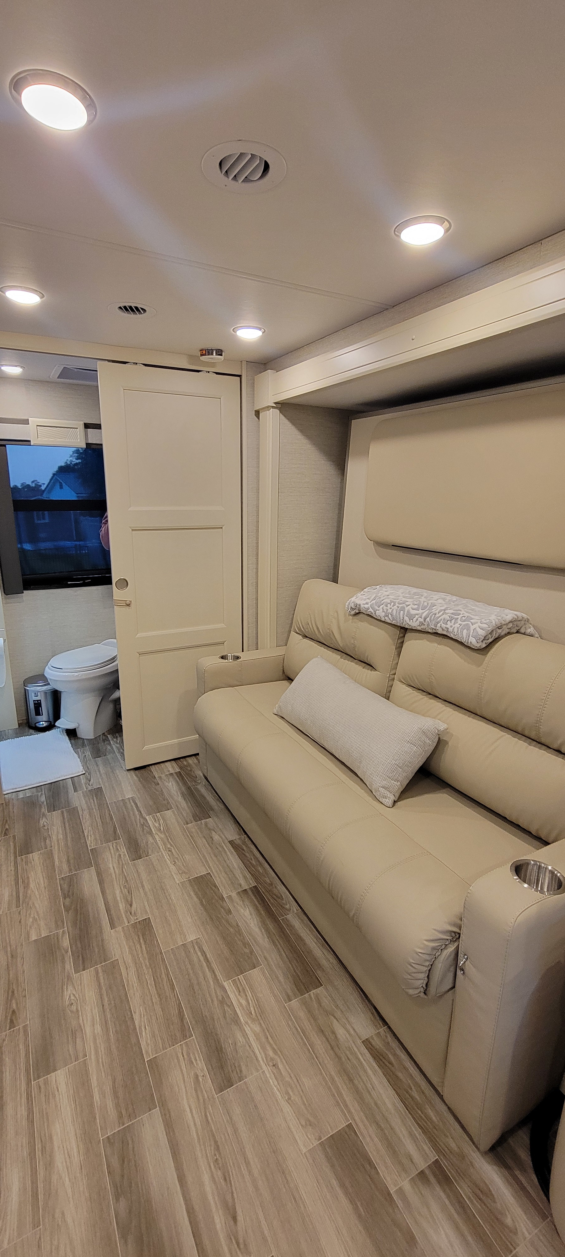Cozy RV rental living area with a plush sofa, wood-look floor, and bathroom access. Ideal for comfortable travel.. Wayfarer Wayfarer Motorhome 2024