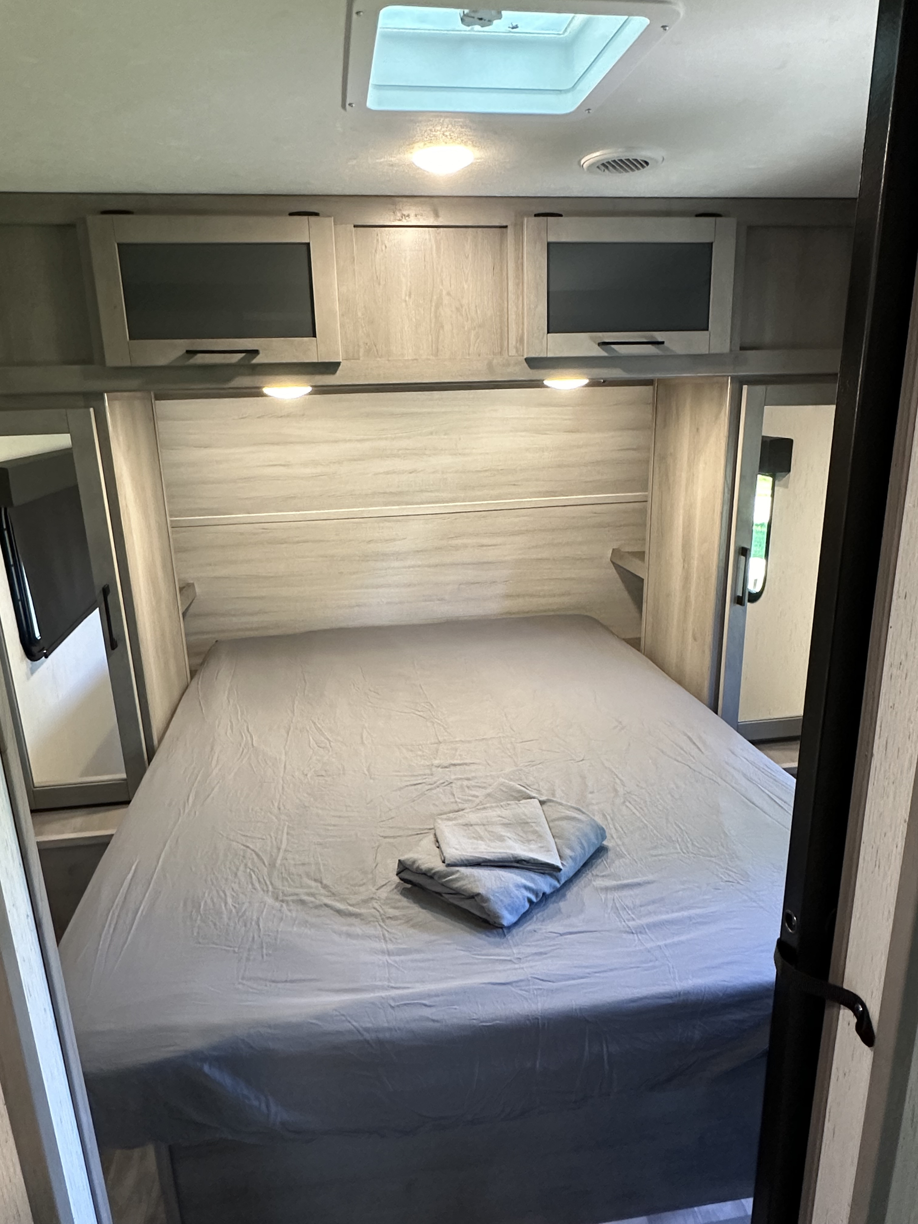 Cozy RV rental bedroom with a made bed, overhead storage cabinets, and mirrored wardrobes, perfect for compact travel.. Dutchmen Kodiak Ultra Lite 2022