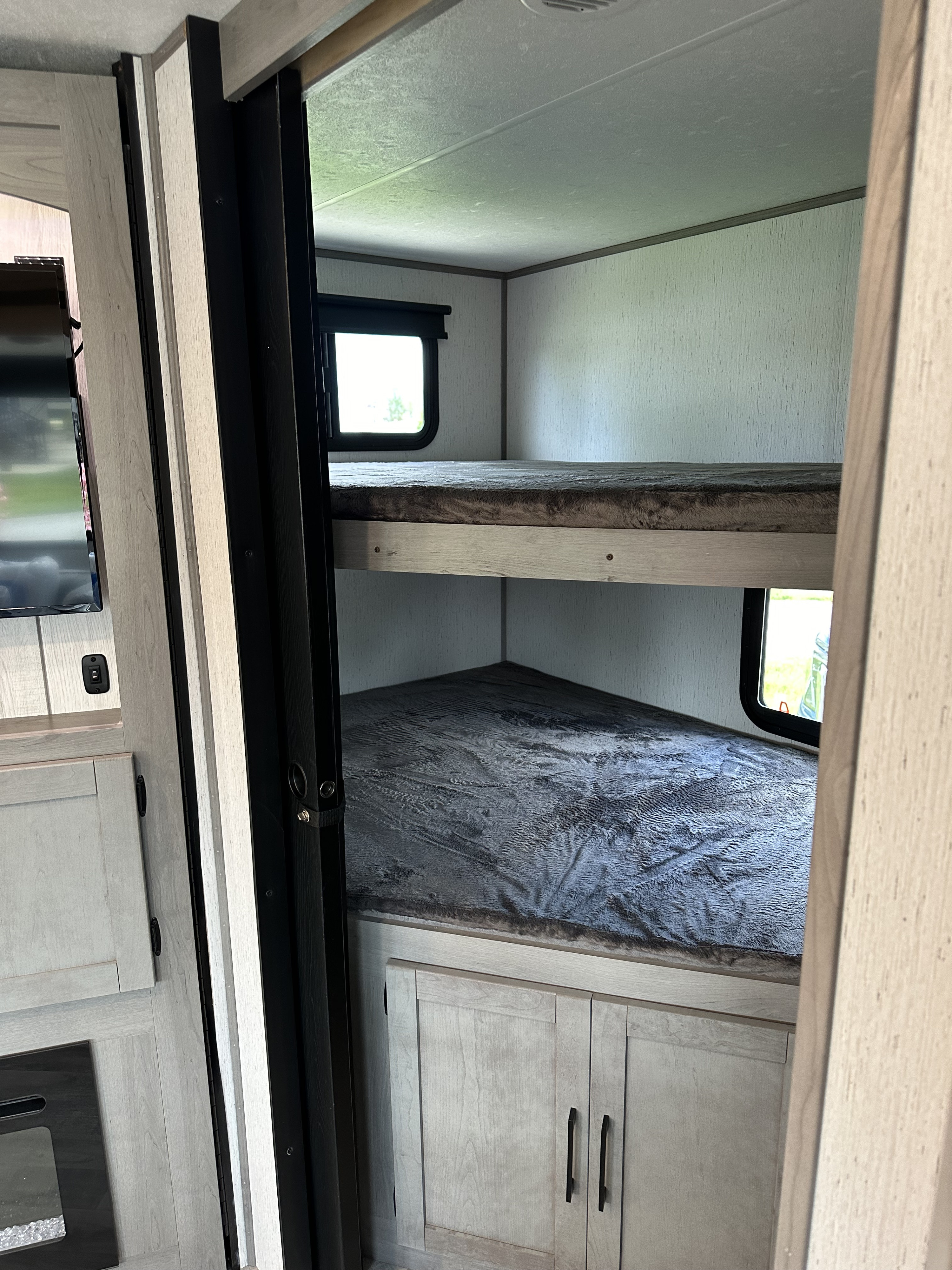 View into an RV rental's bunk room, featuring two cozy beds with blankets, windows, and built-in storage cabinets.. Dutchmen Kodiak Ultra Lite 2022