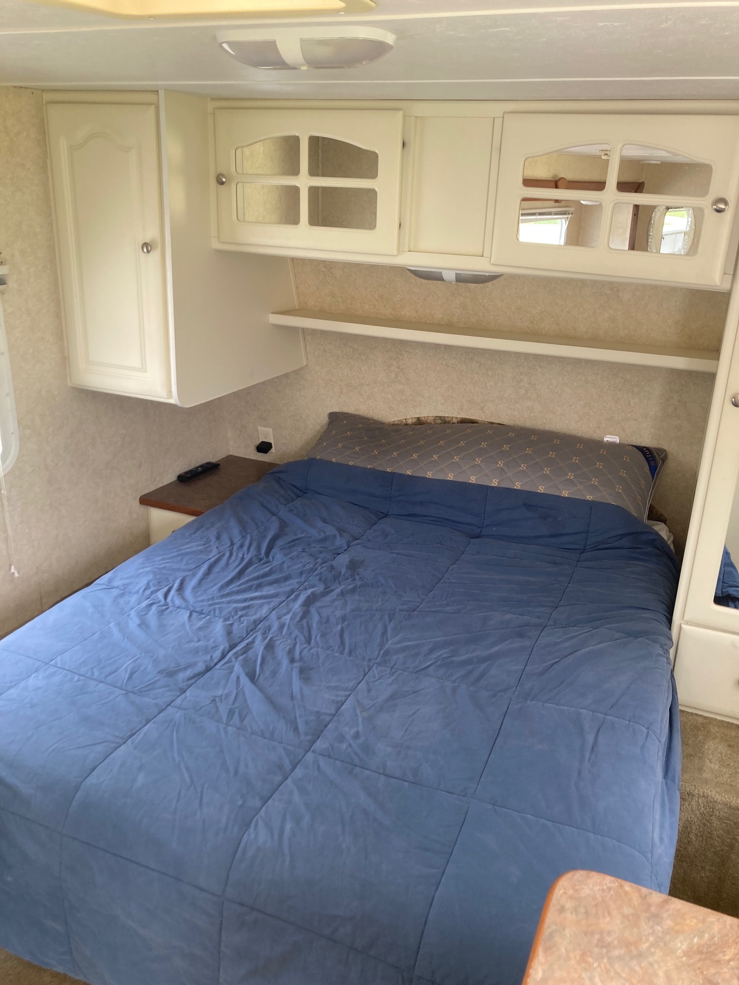 RV rental interior: A cozy bedroom with a blue comforter, white overhead cabinets, and a small nightstand.. Keystone RV Outback 2004
