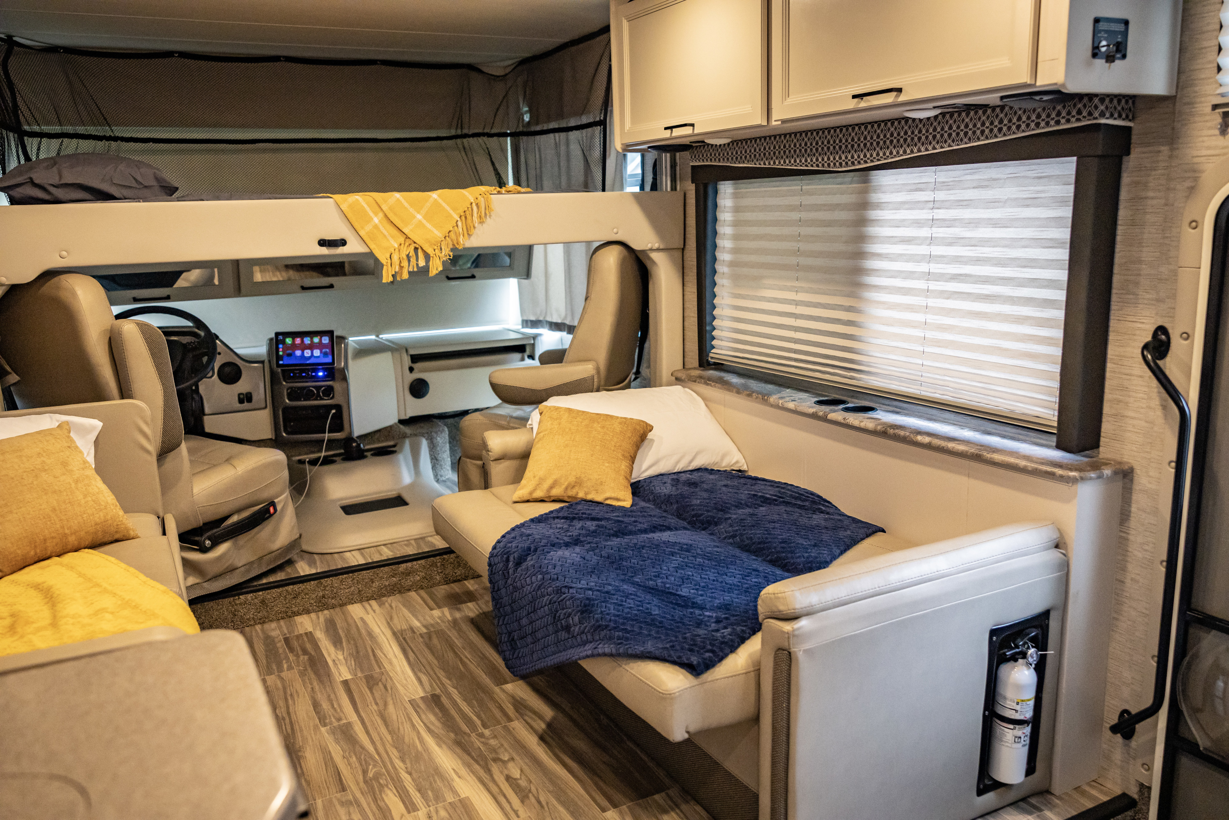 Inside a modern rv rental: bunk bed, driver's cockpit, and convertible sofa with window blinds.. Thor A.C.E. 2023