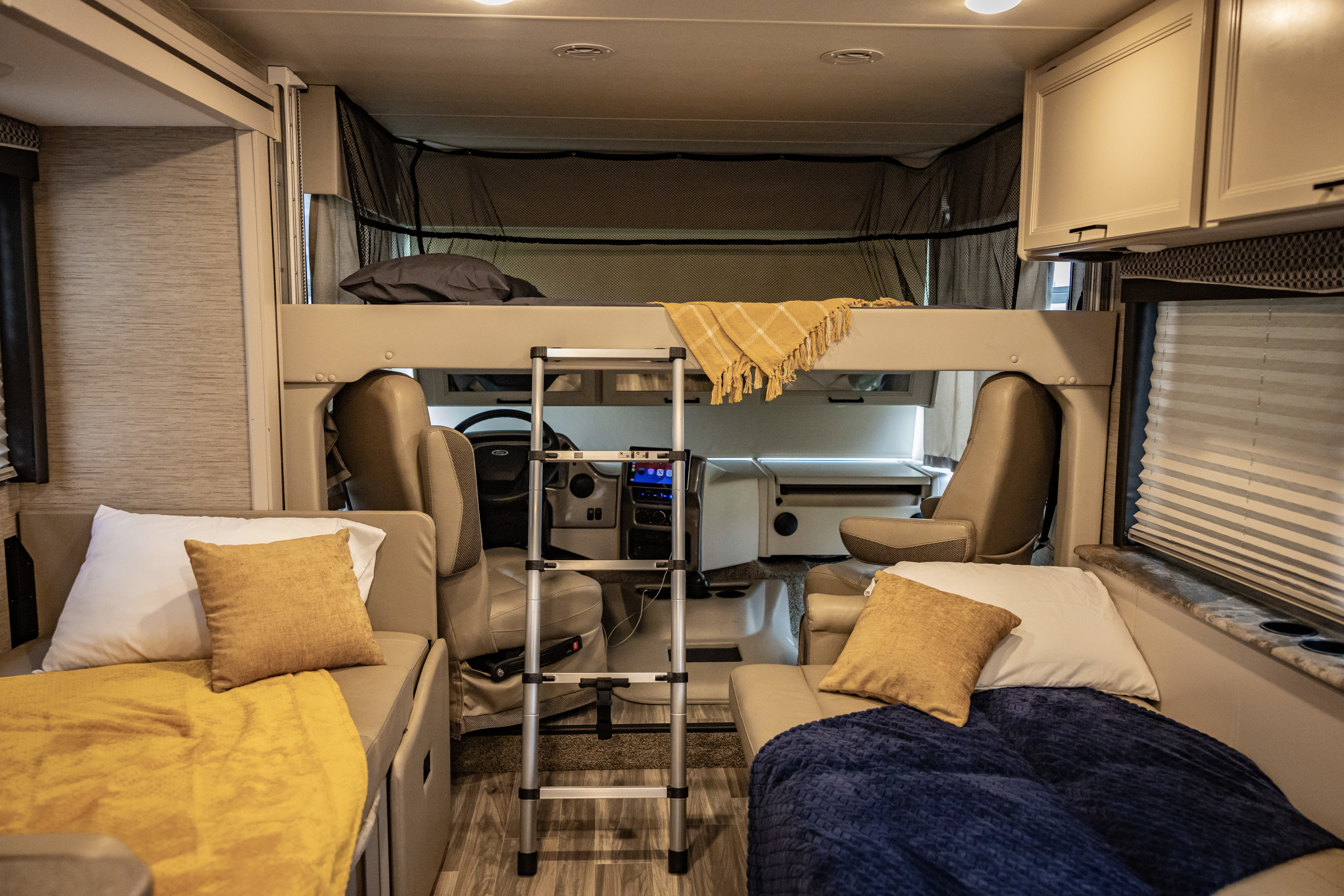 This RV rental interior shows a cab-over bunk, ladder, and two cozy sofa beds, highlighting its versatile living space.. Thor A.C.E. 2023