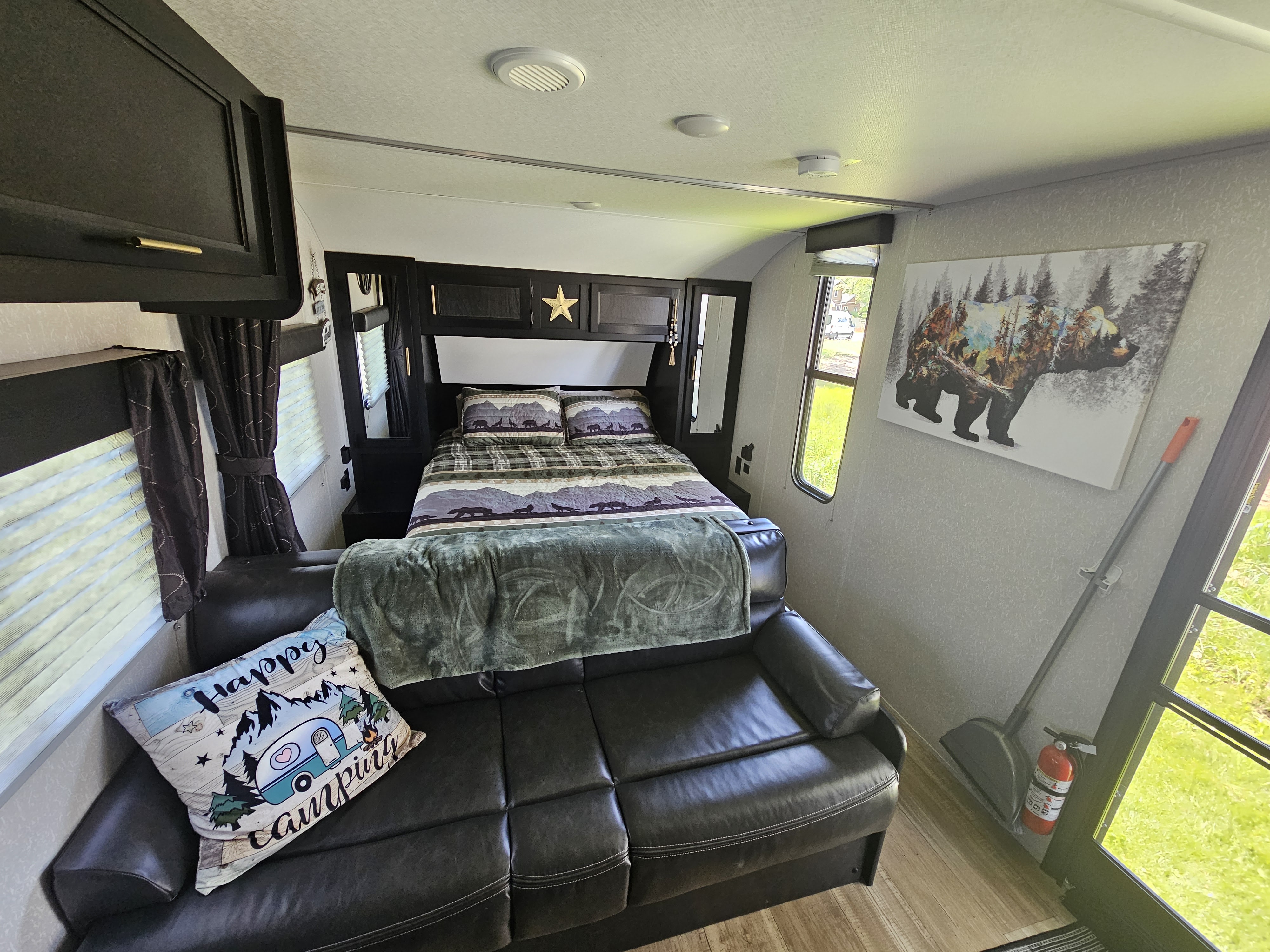 Inside a cozy rv rental bedroom: bear-themed bedding, a sofa with a "Happy Camping" pillow, and outdoor views.. Forest River Cherokee Grey Wolf 2022
