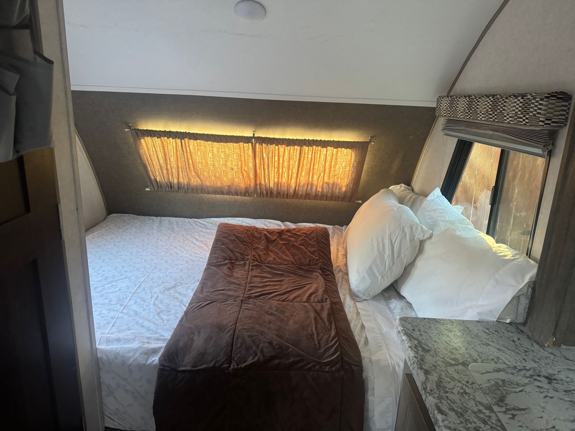 Cozy RV rental bedroom with bed, sunlit windows, curtains, hanging storage, and a small counter area.. R-Pod R-Pod Trailer 2018