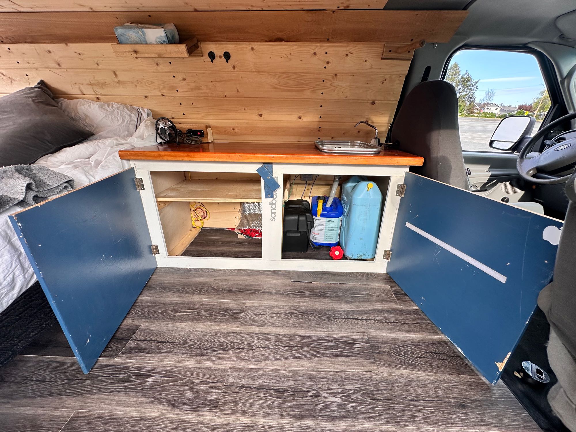 Inside a custom rv rental camper van, showing the bed, wood counter with sink, and open storage for mobile living.. Ford Econolline 250 2005
