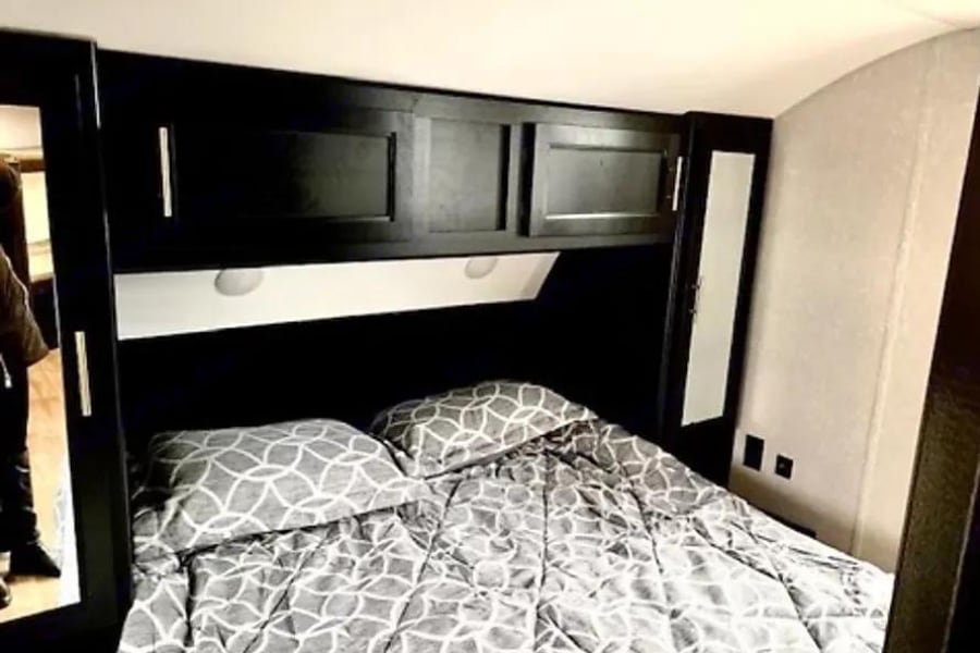 Cozy RV rental bedroom featuring patterned gray bedding, overhead cabinets, and mirrored wardrobes, ideal for compact travel.. Forest River Cherokee Grey Wolf 2022