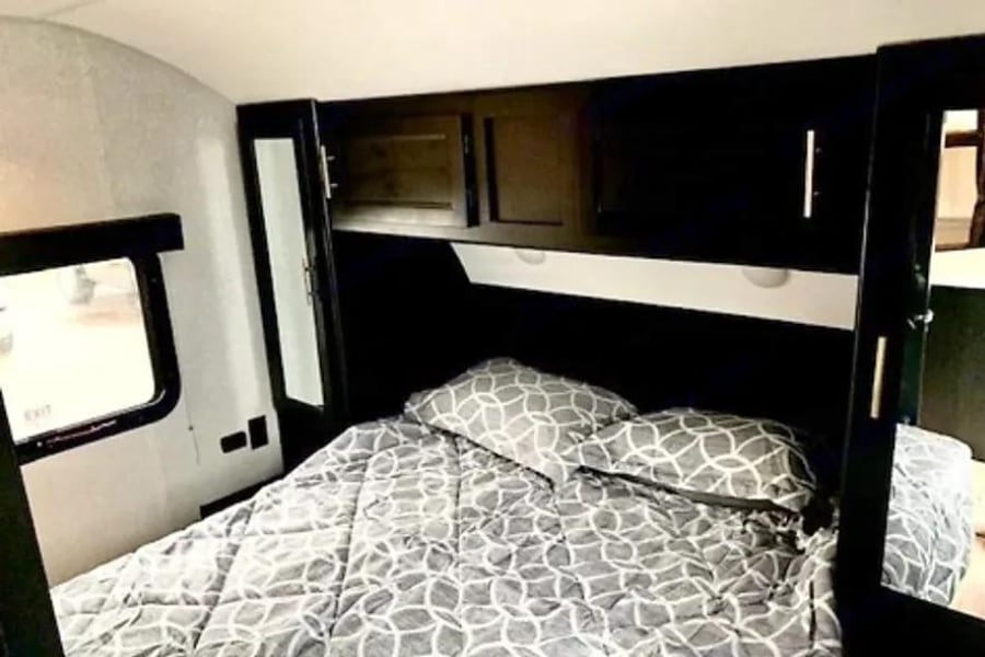 Cozy RV rental bedroom with a patterned bed, overhead cabinets, and a window, perfect for your next adventure.. Forest River Cherokee Grey Wolf 2022