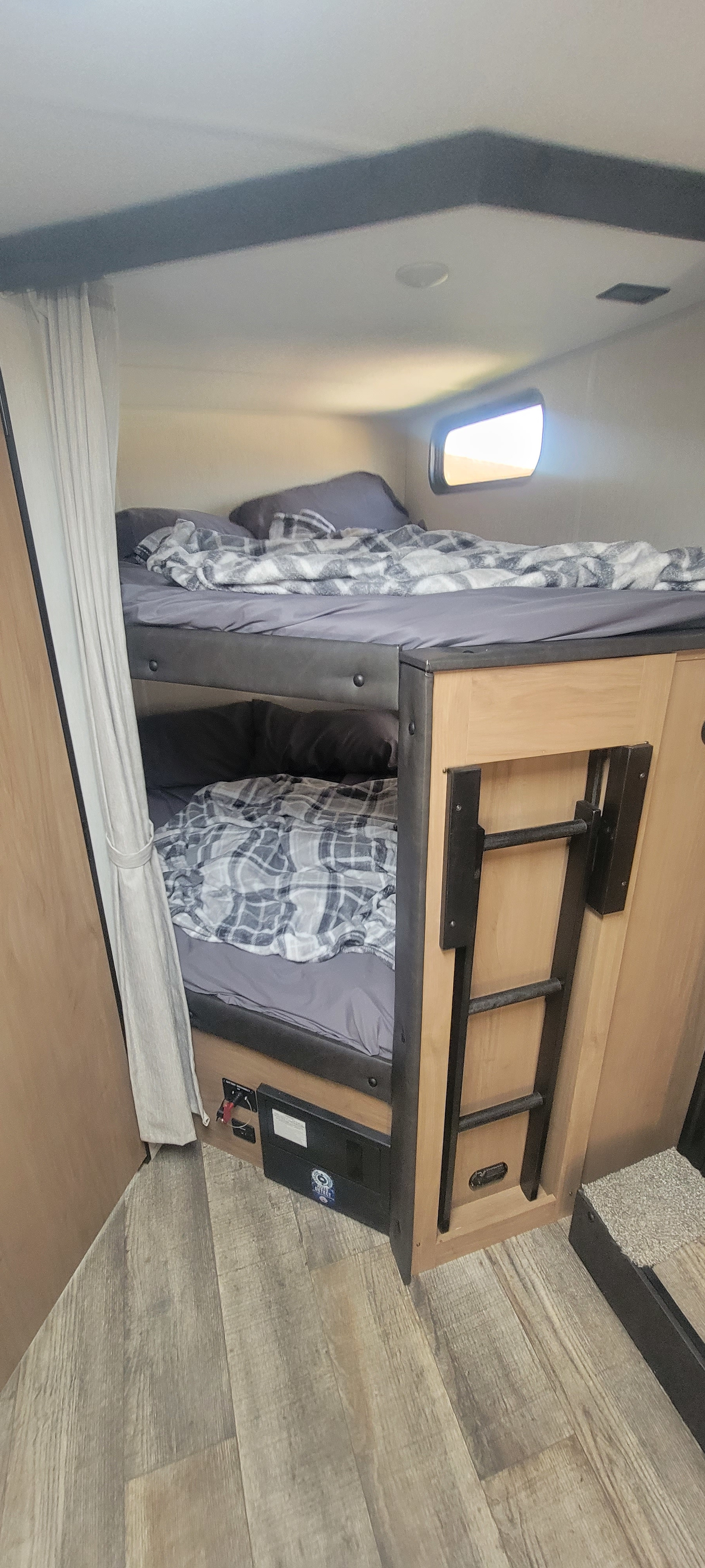 This **rv rental** showcases compact bunk beds with plaid blankets, a ladder, an electrical panel, and wood-look flooring.. Forest River Cherokee Grey Wolf 2023
