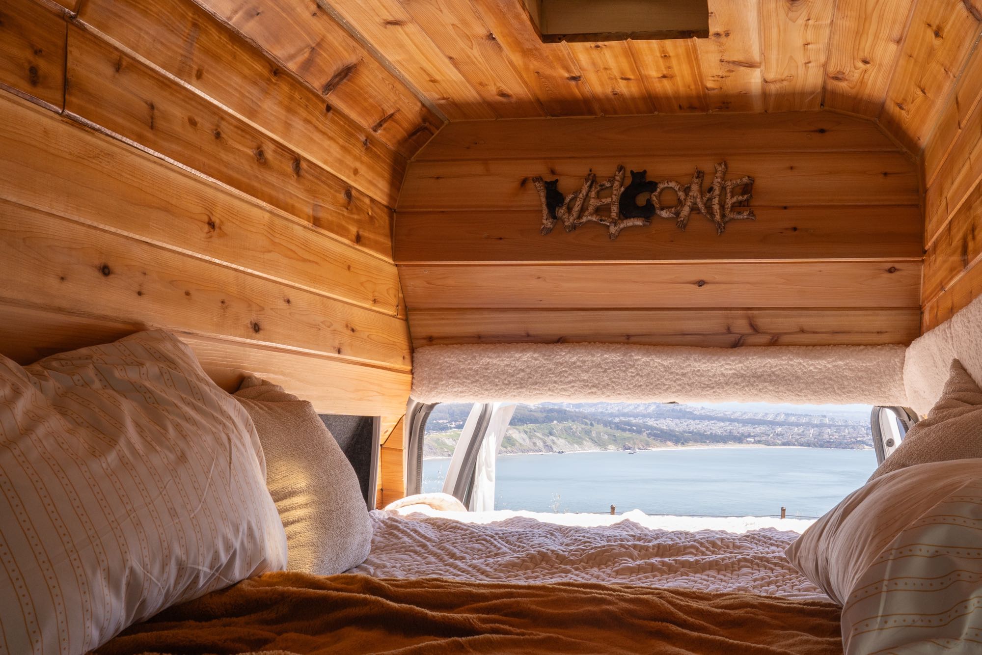 Cozy RV rental interior featuring a wood-paneled bedroom with a "WELCOME" sign and a scenic ocean and city view.. Ford Econoline 2011