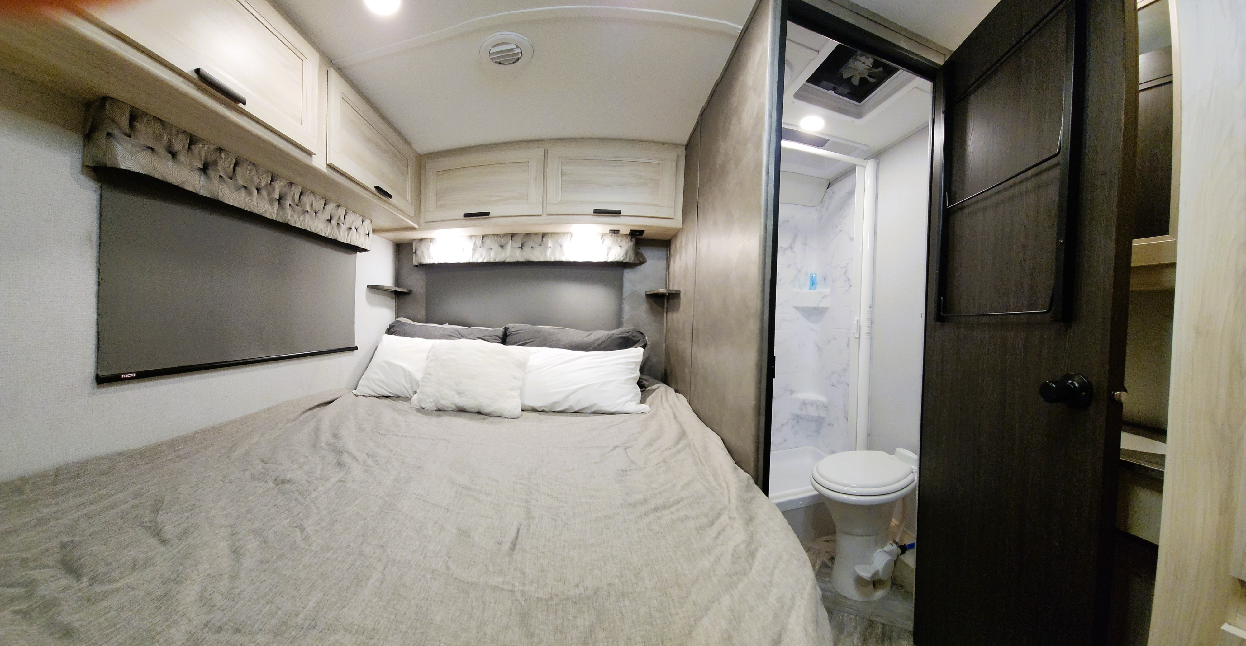 RV rental bedroom features a comfortable bed with overhead storage and an adjacent compact bathroom with a toilet and shower.. Forest River Sunseeker LE 2022