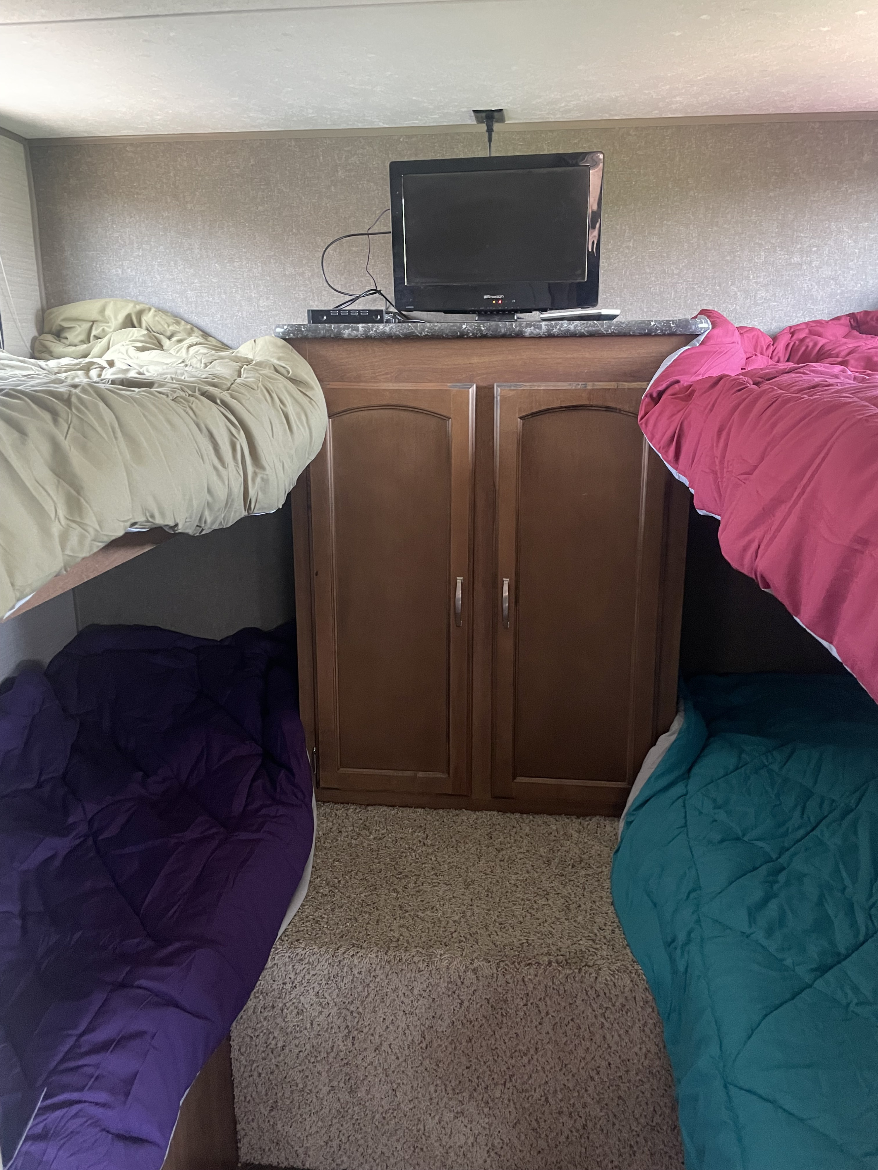 An RV rental bunkhouse: Four colorful bunk beds (two upper, two lower) surrounding a central cabinet with a TV.. Keystone RV Springdale 2016