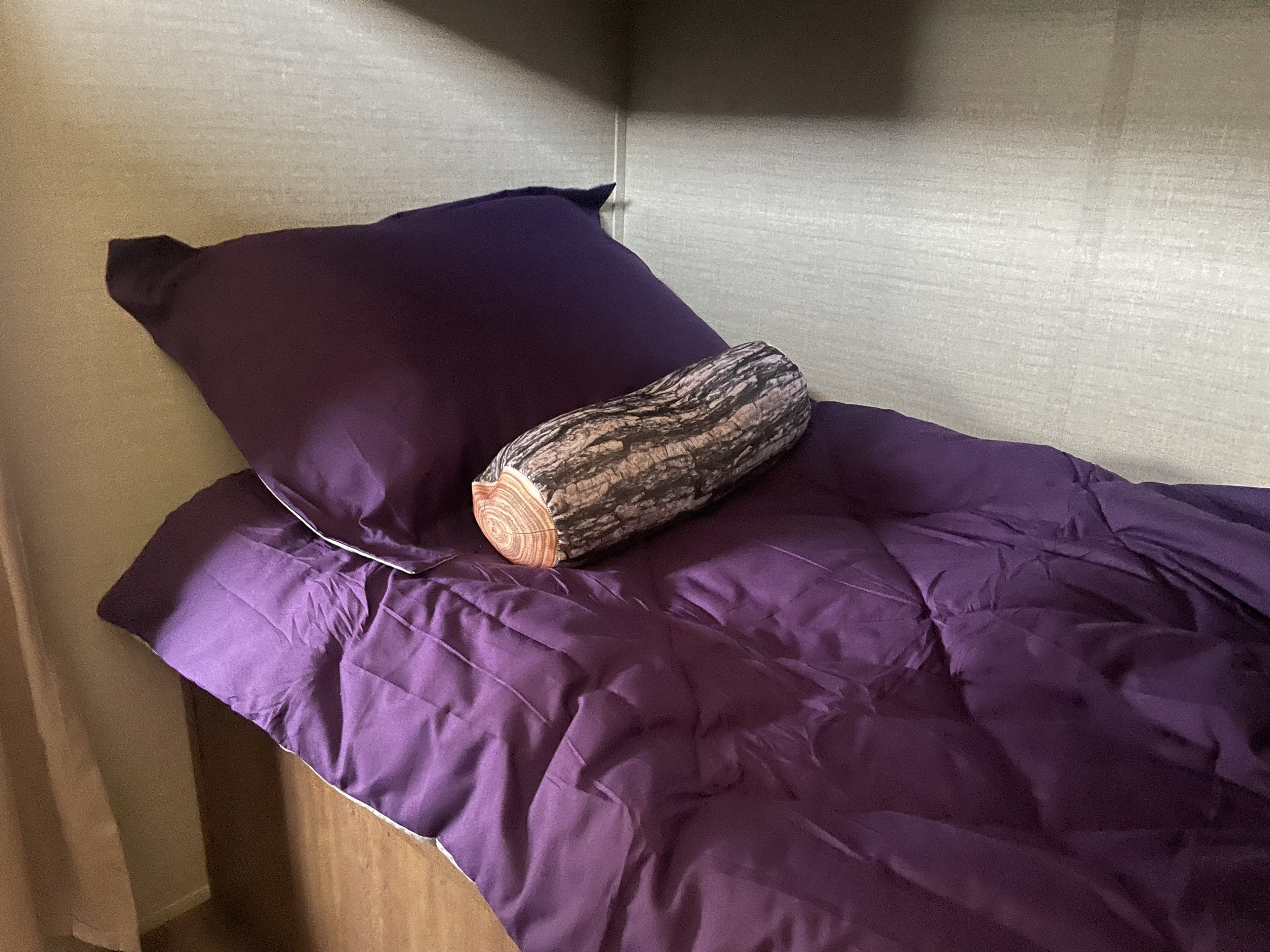 Cozy purple bed with a log pillow in an RV rental, offering comfortable sleeping for your travels.. Keystone RV Springdale 2016