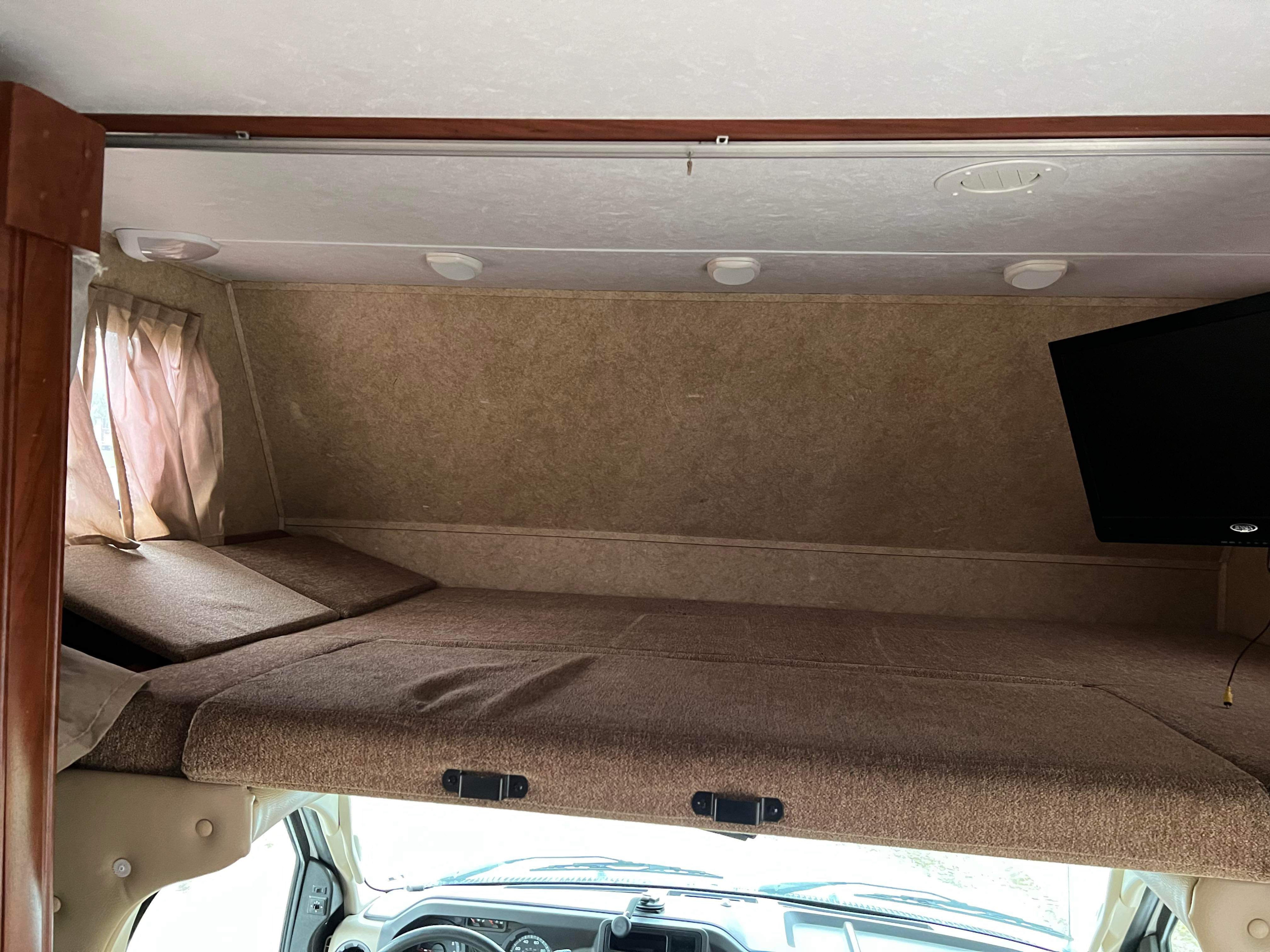 RV rental interior: a comfy cab-over bunk bed with cushions, window curtains, and a TV, ideal for relaxing on your trip.. Forest River Sunseeker 2013