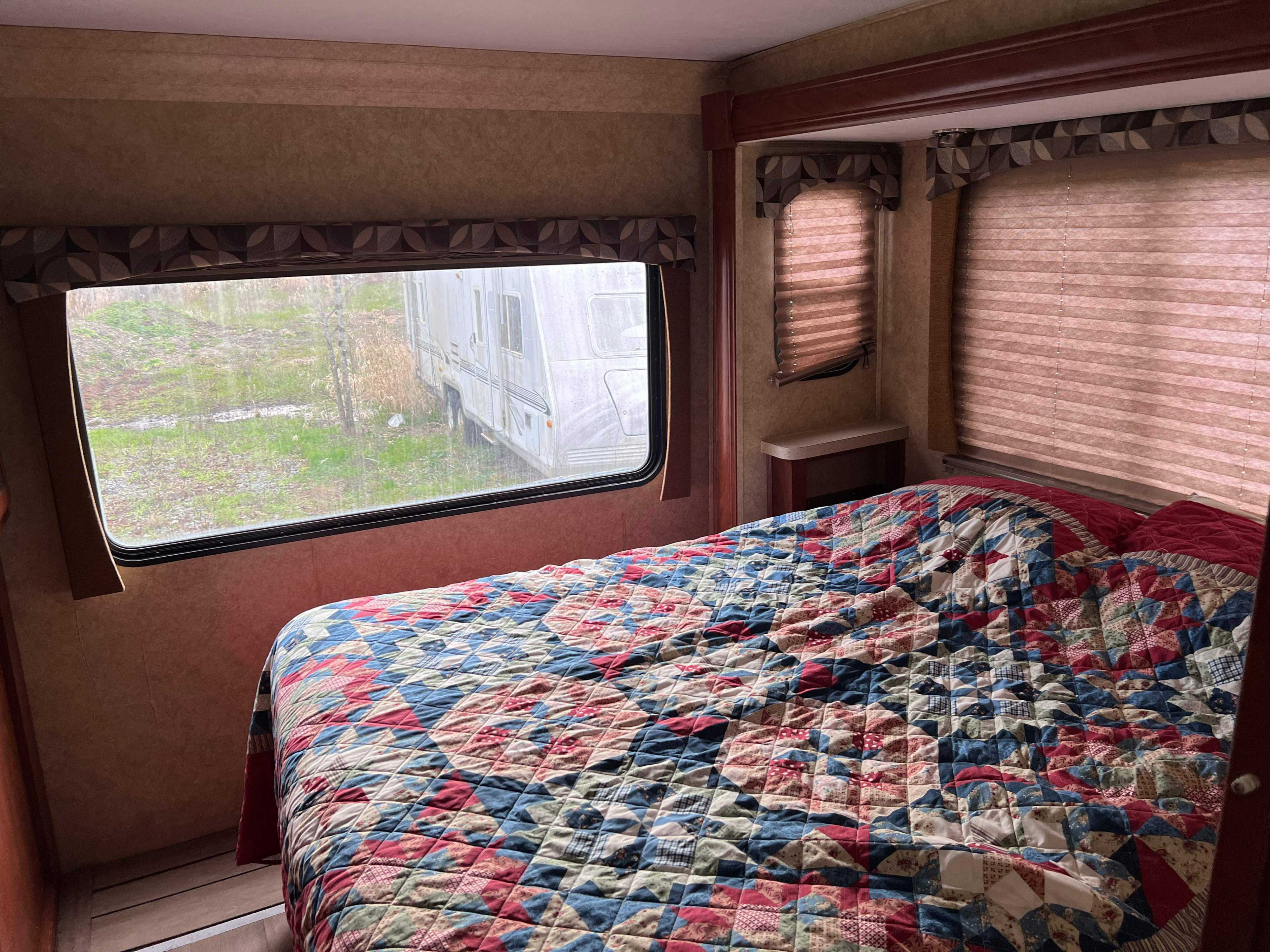 Cozy RV bedroom for your next RV rental adventure, featuring a patchwork quilt and scenic window view.. Forest River Sunseeker 2013