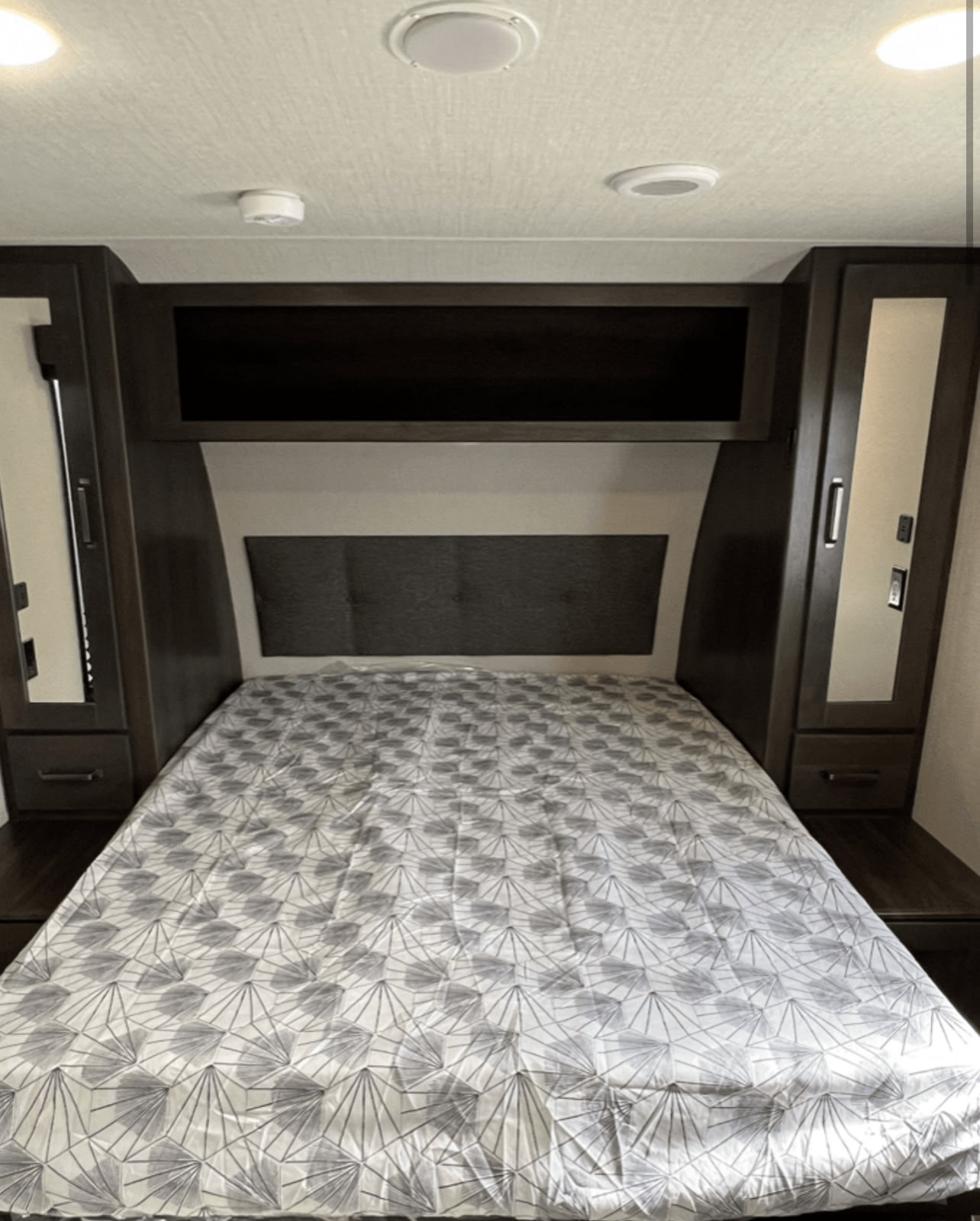 RV rental bedroom featuring a bed with patterned comforter, upholstered headboard, and dark wood storage.. Xplorer transcend 2024