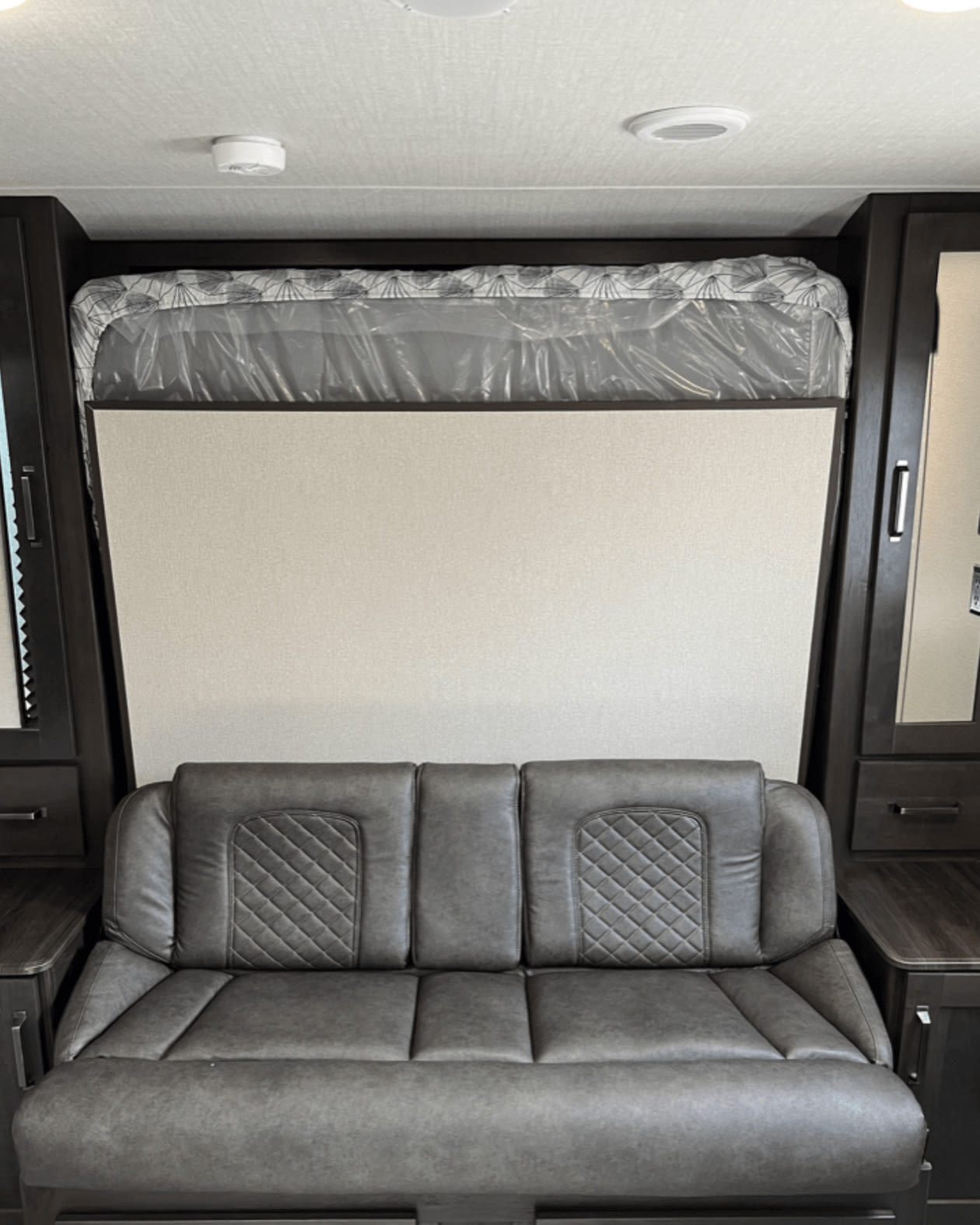 RV rental: Compact interior showing a grey sofa and a bed with mattress still in plastic, above dark wood cabinets.. Xplorer transcend 2024