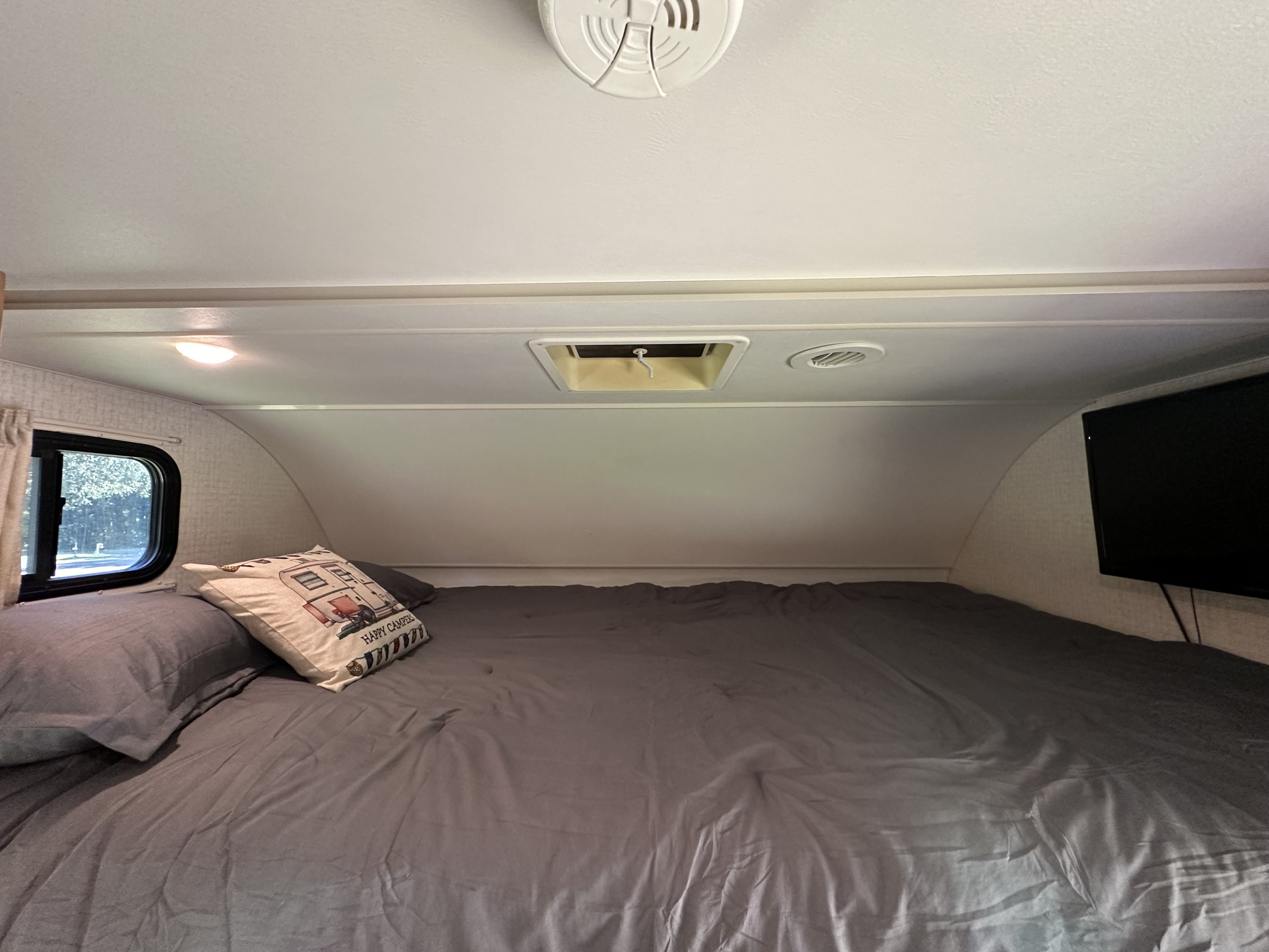 Inside an RV rental: a cozy bedroom with gray bedding, a window, TV, and overhead features for comfortable stays.. Winnebago Spirit 2017