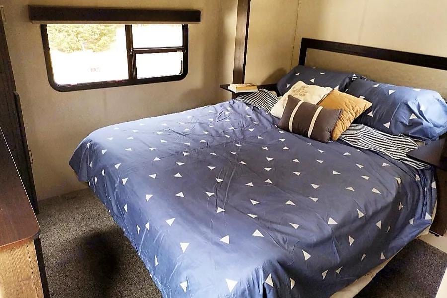 Comfortable RV rental bedroom: blue bedding, assorted pillows, and a window for scenic views on your travels.. Forest River Hemisphere 2018