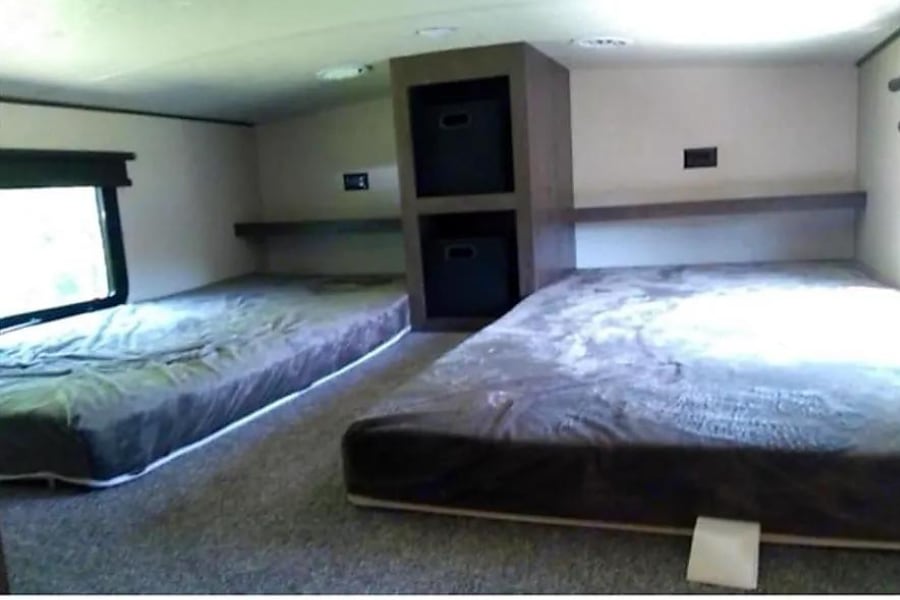 Inside an RV rental bunkhouse: two floor mattresses on carpet, separated by a central storage unit with bins. Ready for travel.. Forest River Hemisphere 2018