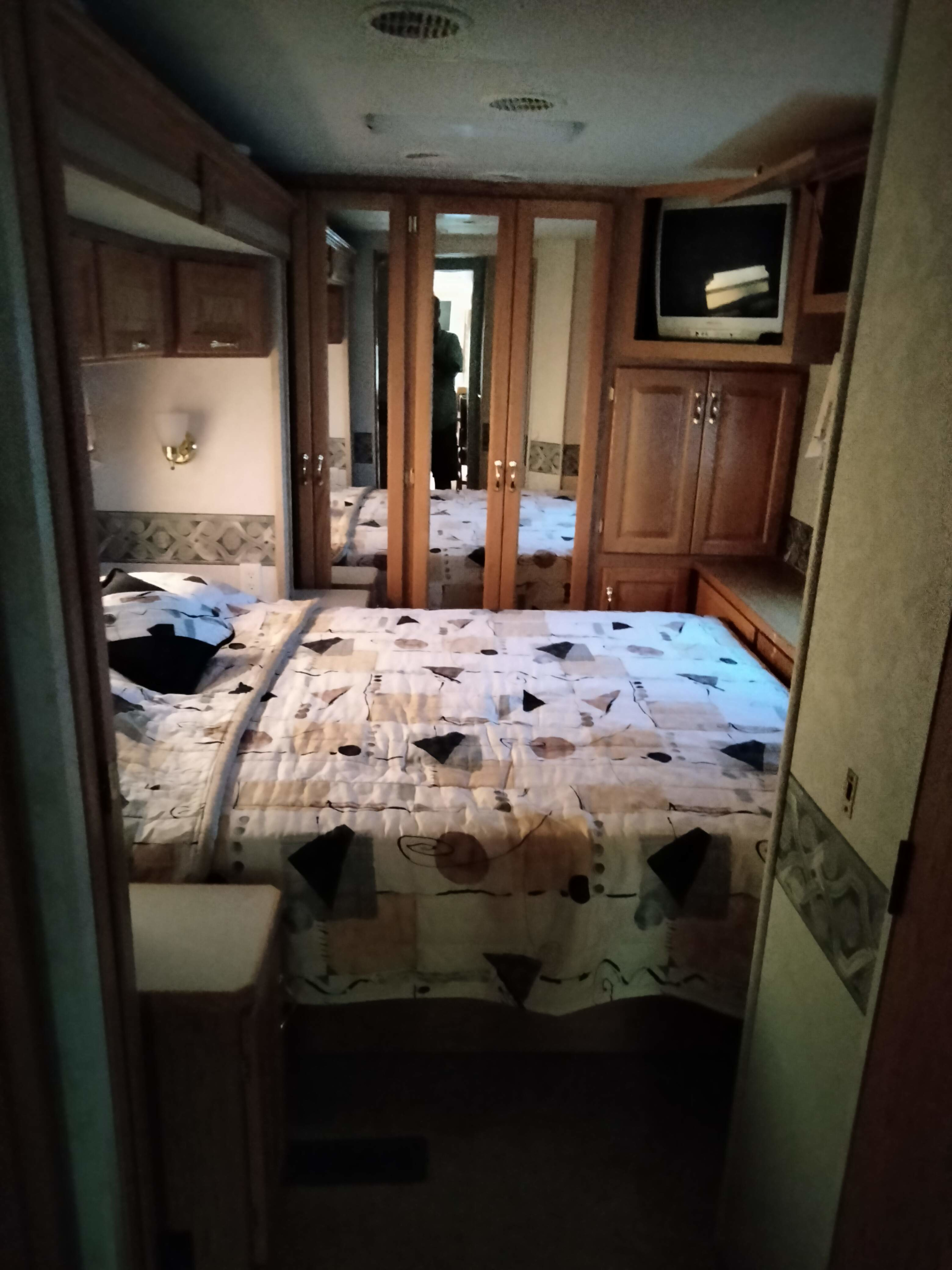Cozy RV rental bedroom featuring mirrored closets, a TV, and a patterned bed.. Newmar Kountry Star 2004