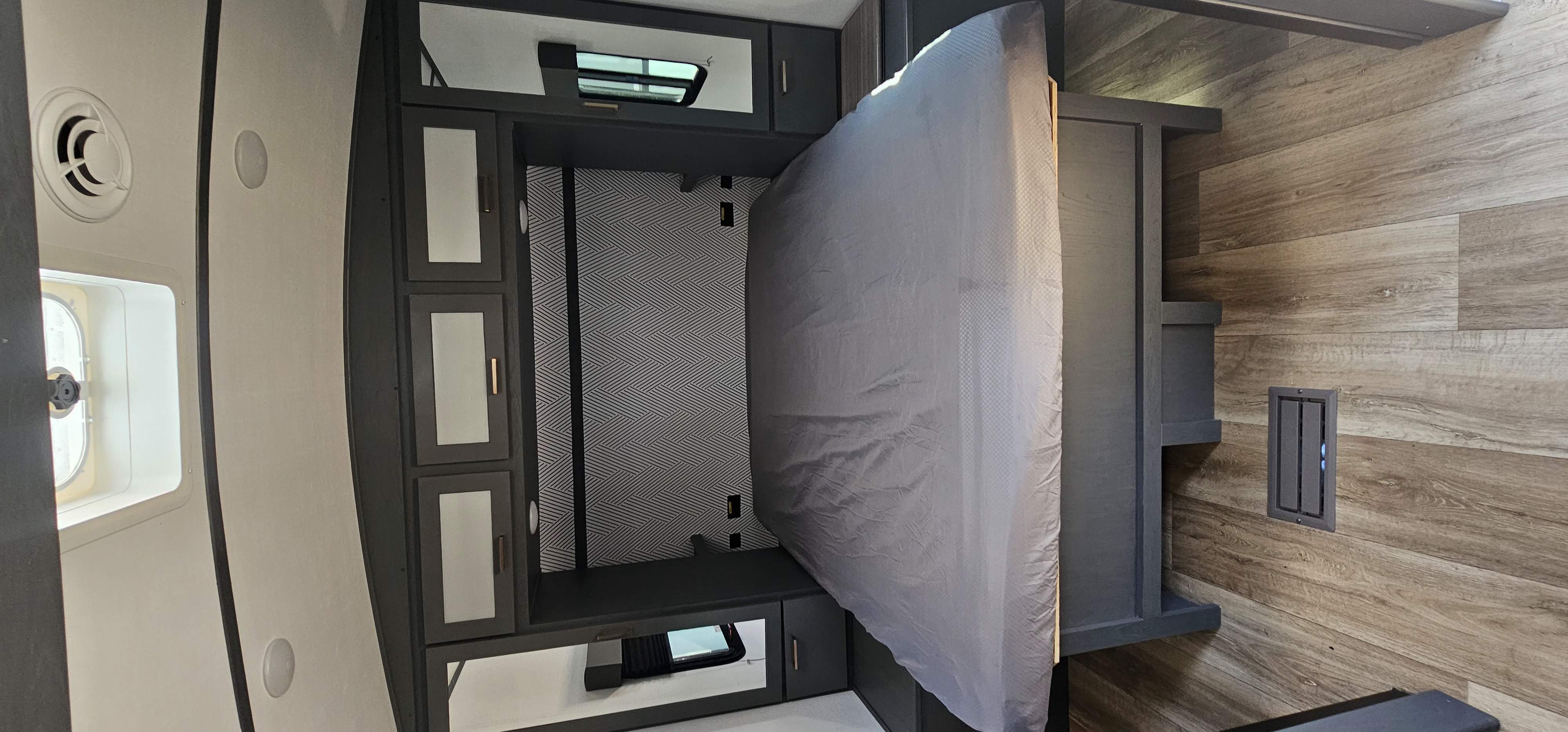 RV rental interior: Bedroom with an upright bed, dark built-in cabinetry, and a modern patterned accent wall for smart storage.. Keystone RV Bullet Ultra Lite 2023