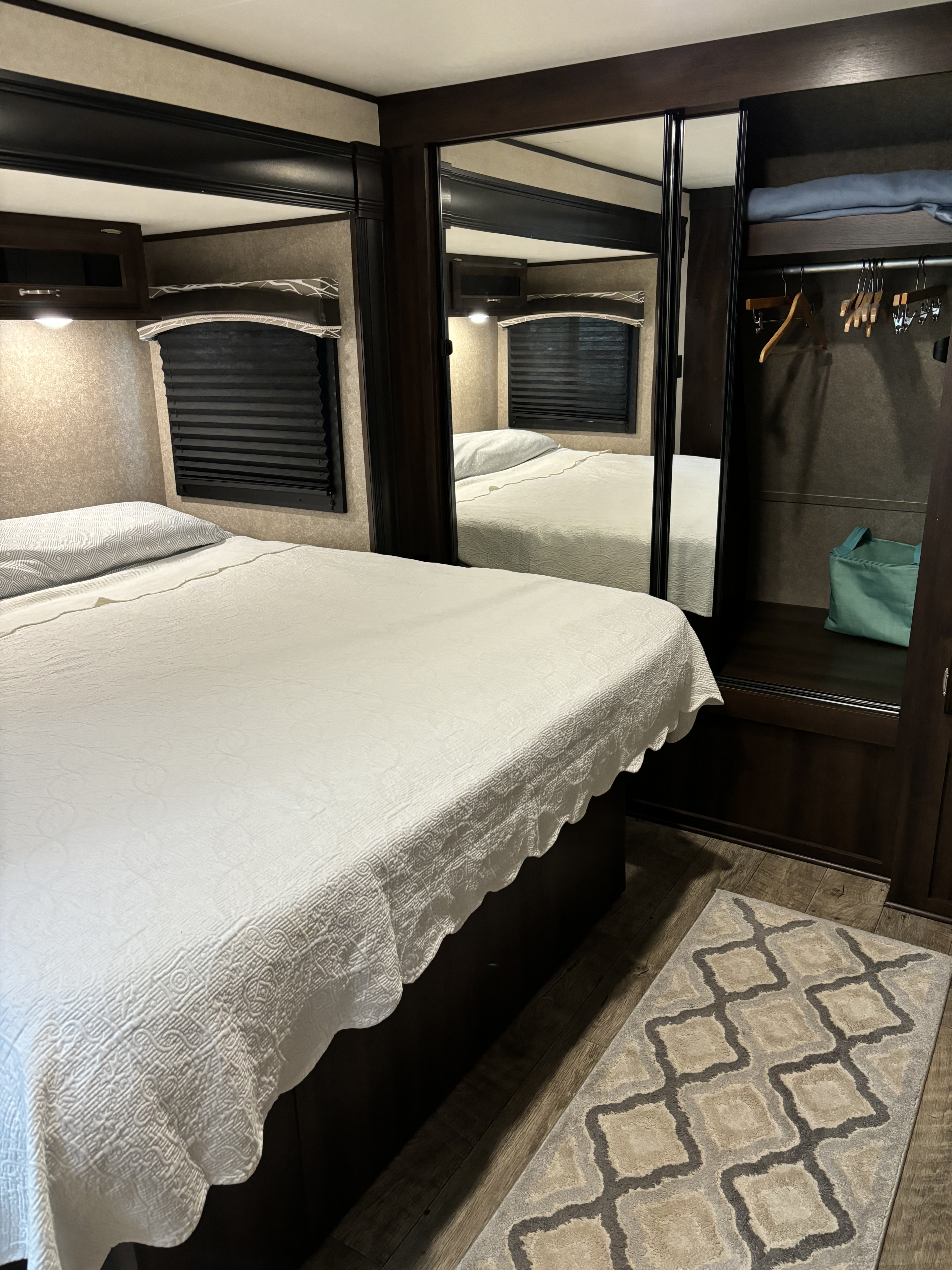 Cozy RV rental bedroom with white bedding, dark wood accents, a mirrored closet, and patterned rug. Perfect for travel.. Jayco Jay Flight 2018