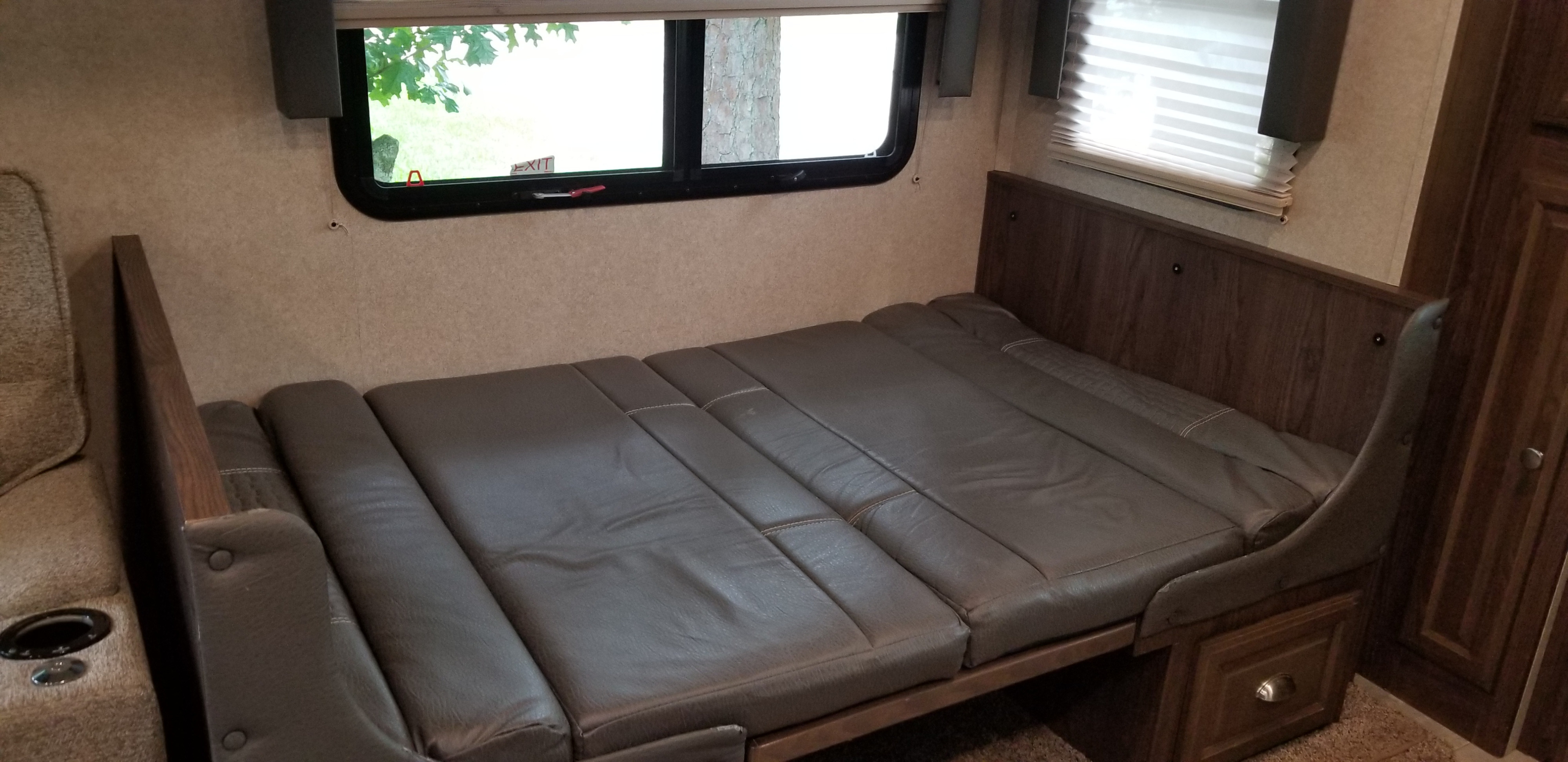 Inside an RV rental: a gray segmented sofa bed is deployed, providing sleeping space next to an emergency exit window.. Forest River Flagstaff Classic Super Lite 2018