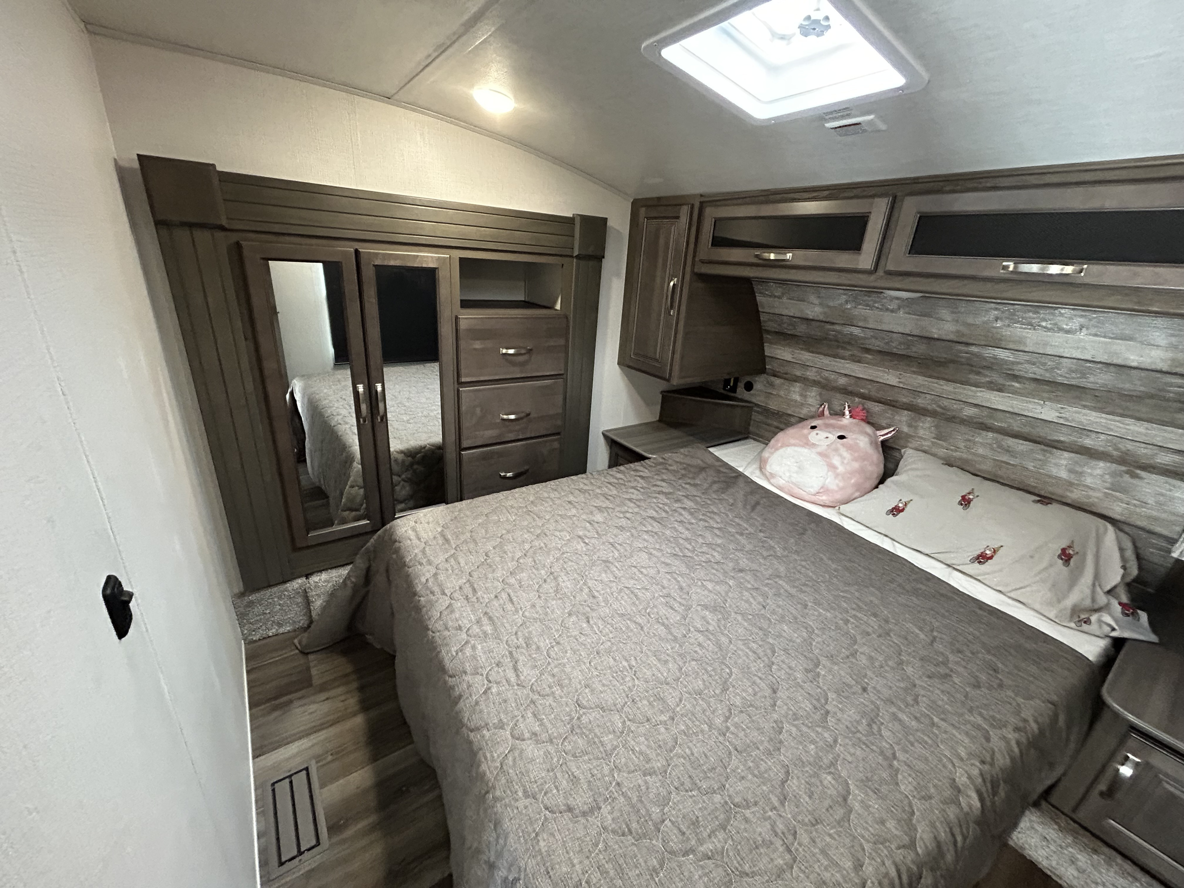 Cozy RV rental bedroom with a neatly made bed featuring a gray quilt, built-in storage, and a bright skylight.. Keystone RV Cougar 2023
