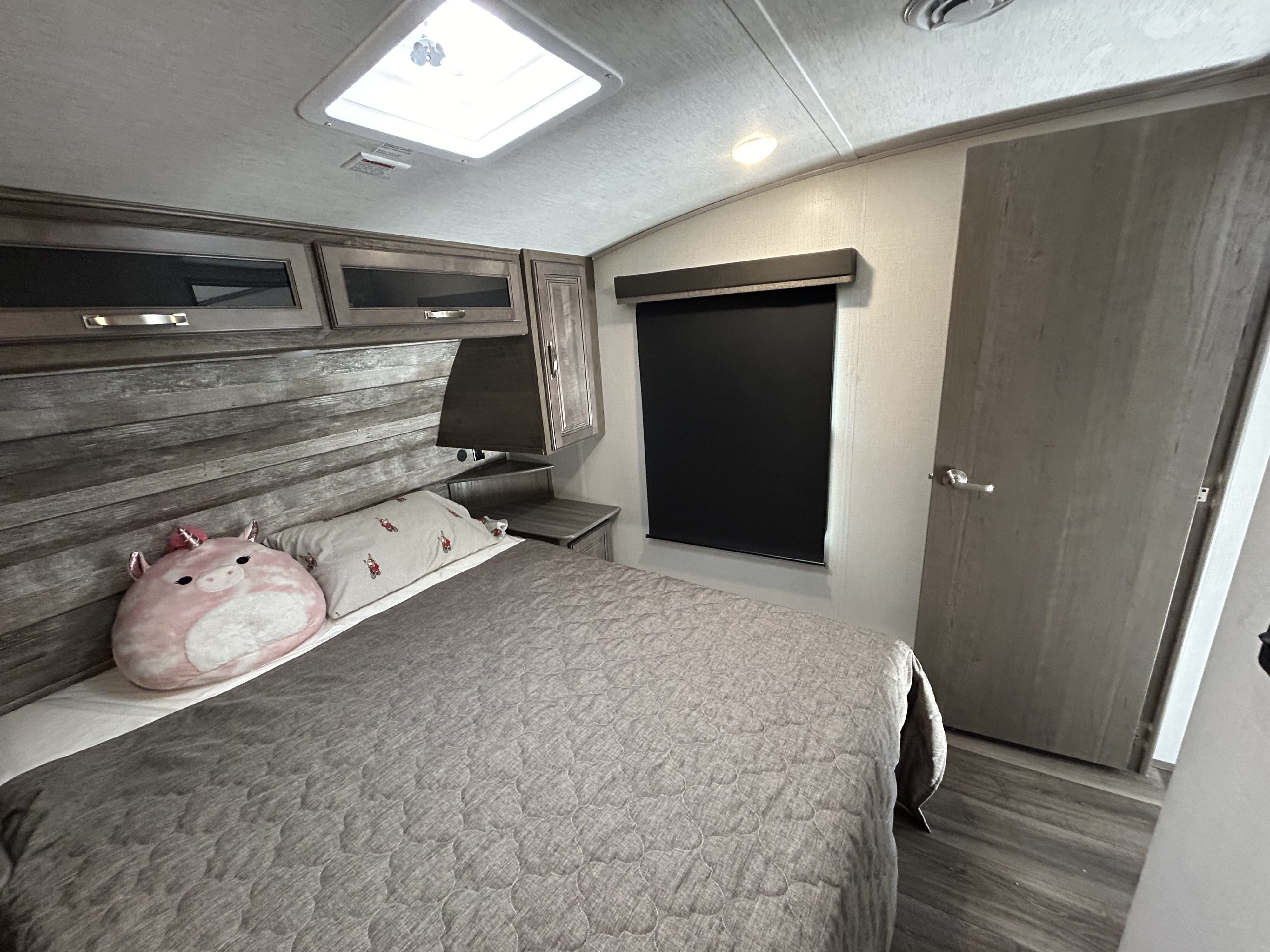 Comfortable RV rental bedroom with a bed, unicorn pillow, wood-look cabinets, and a ceiling skylight.. Keystone RV Cougar 2023