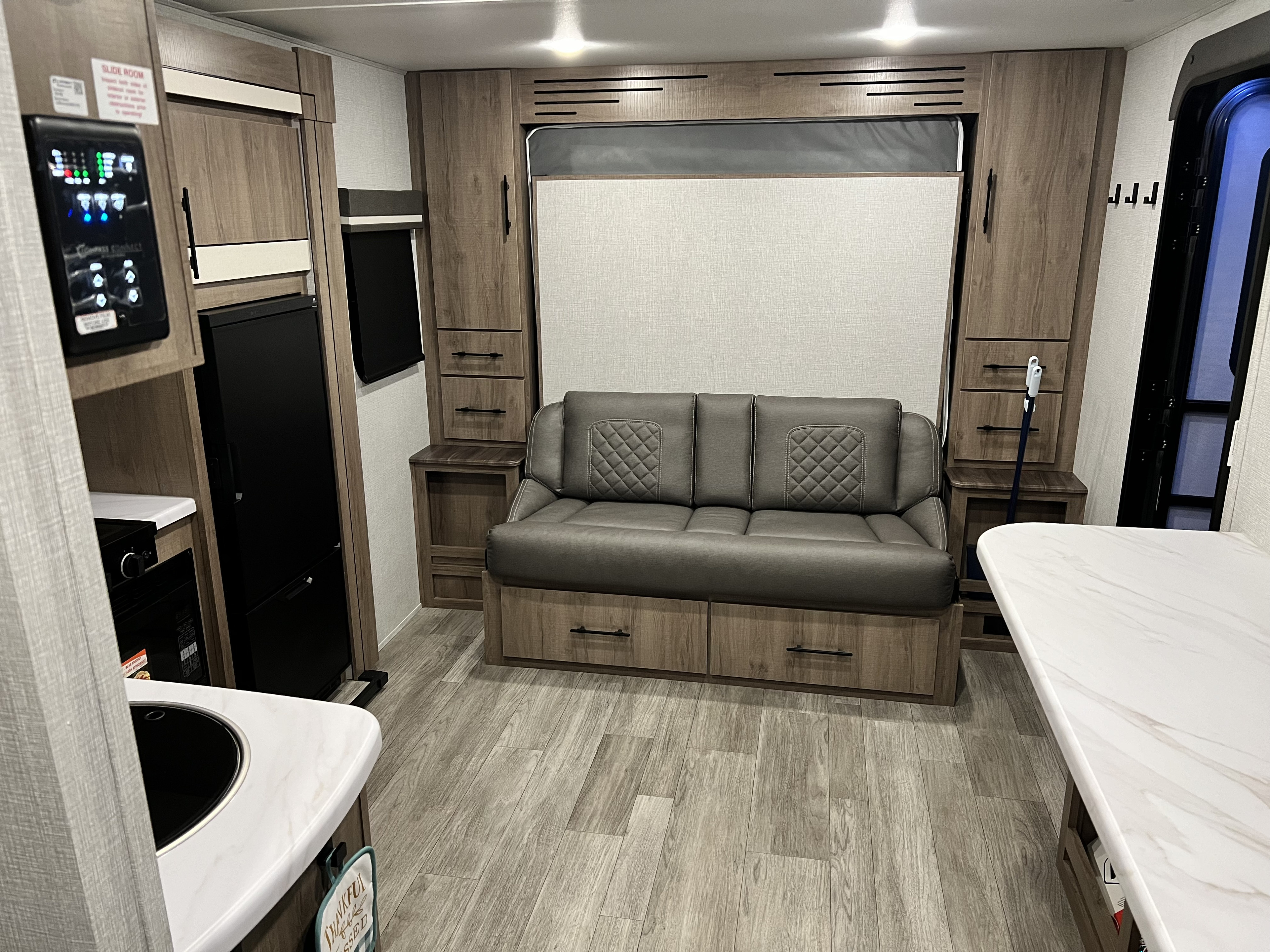 Inside a stylish RV rental: grey sofa, compact kitchen, smart control panel, and ample wood-look cabinetry.. Grand Design Imagine 2023