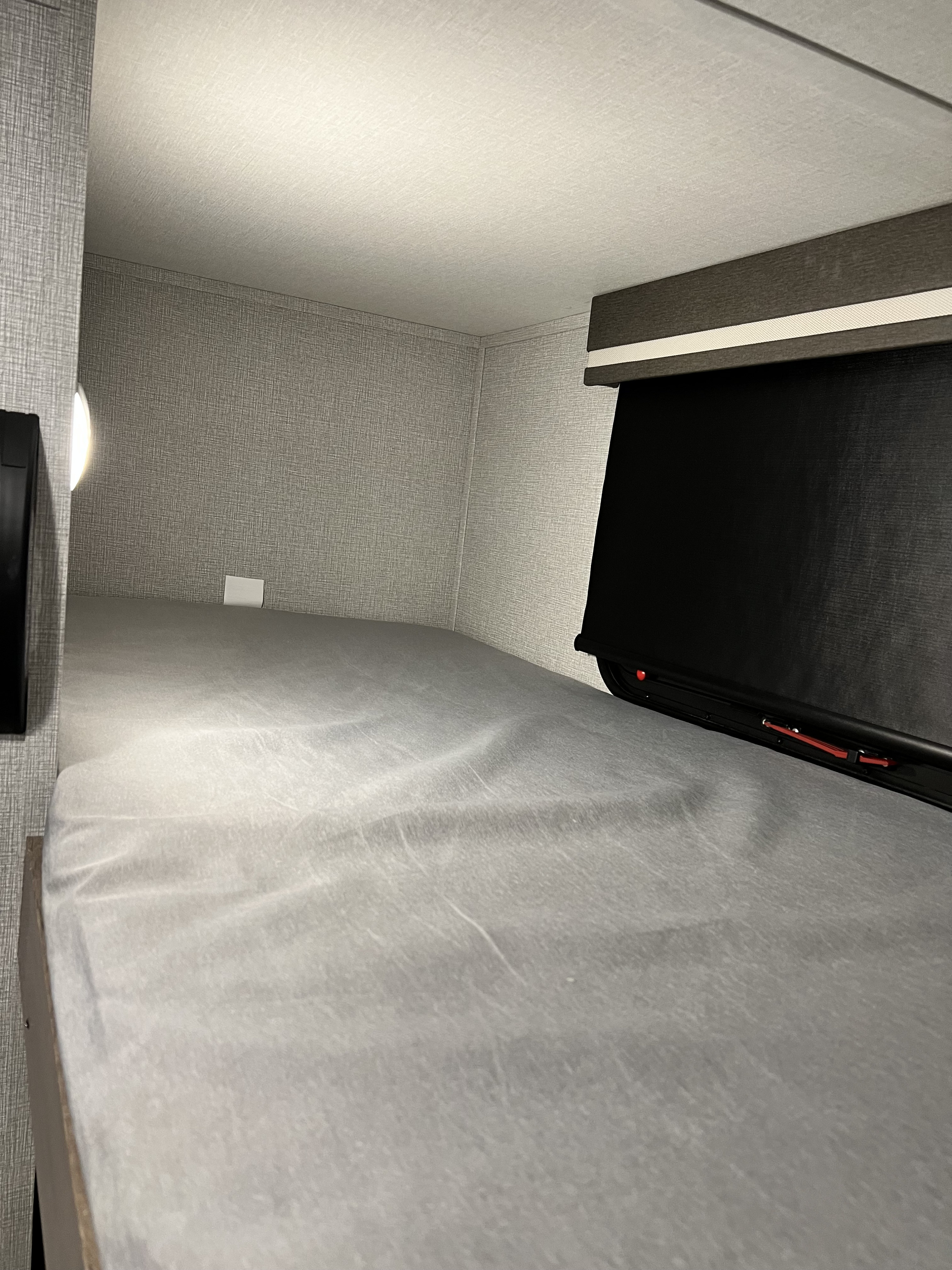 RV rental bunk: cozy sleeping area with grey interior, window blind, reading light, and power outlet.. Grand Design Imagine 2023