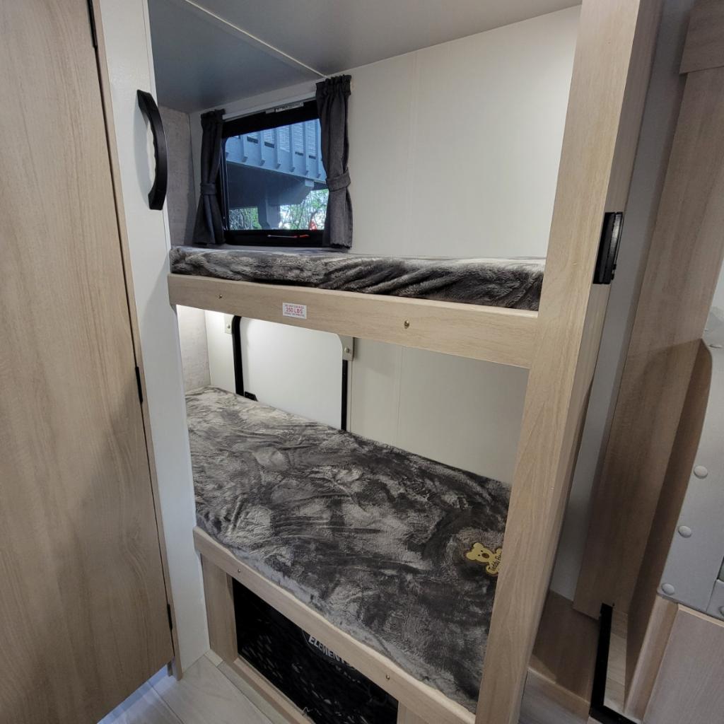 Modern RV rental interior: two cozy bunk beds with gray blankets and a window, offering practical sleeping space.. Minnie Micro Minnie 2023