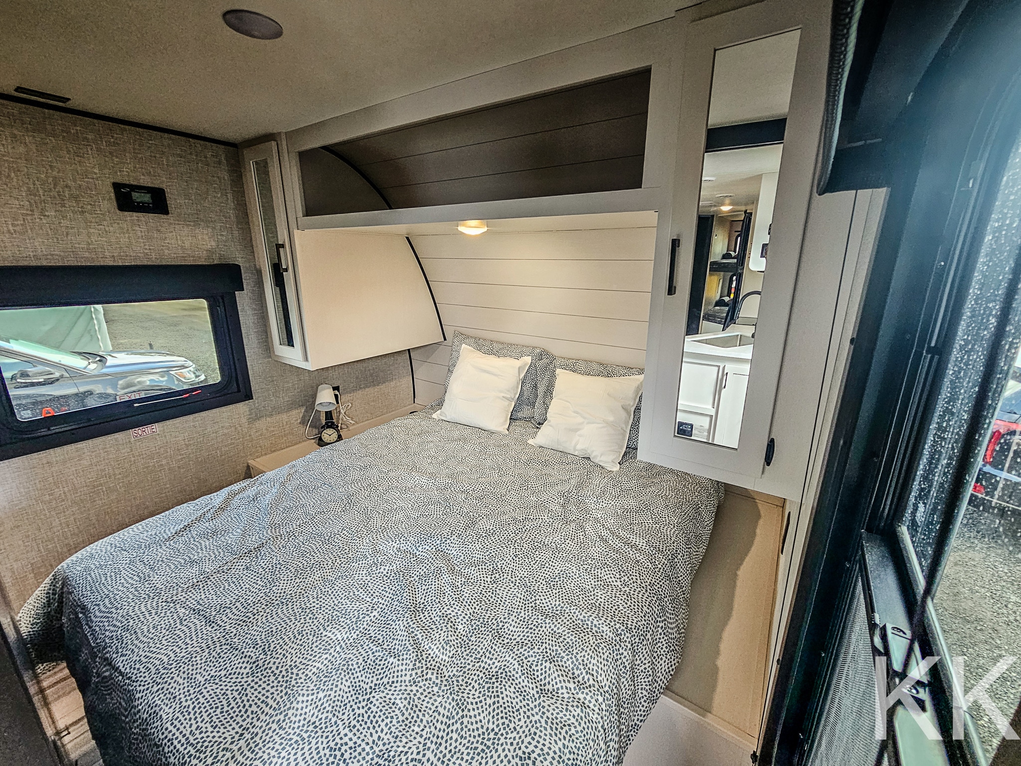 Cozy RV rental bedroom with patterned bedding, bedside lamp, and mirrored storage, offering comfort on the road.. Highland Ridge RV Open Range 2024